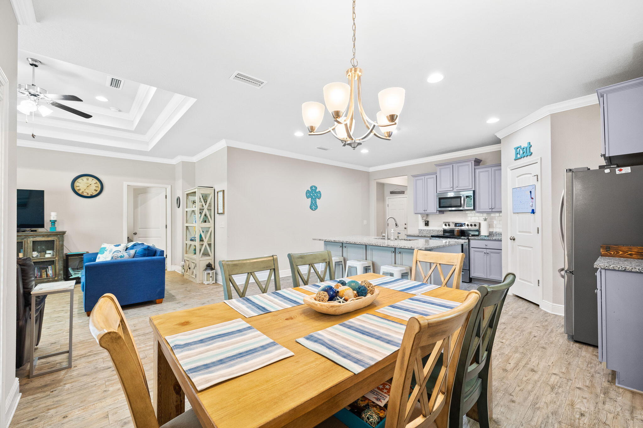 Open-plan dining area with a wooden table beneath a chandelier, beside a lavender-and-blue kitchen.