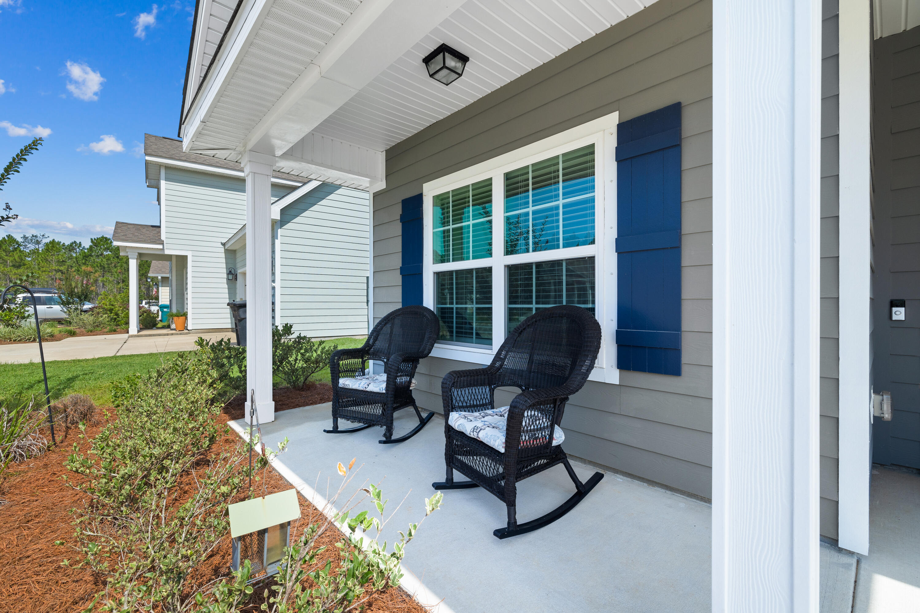 Covered porch with two black wicker rocking chairs beside a window with blue shutters.