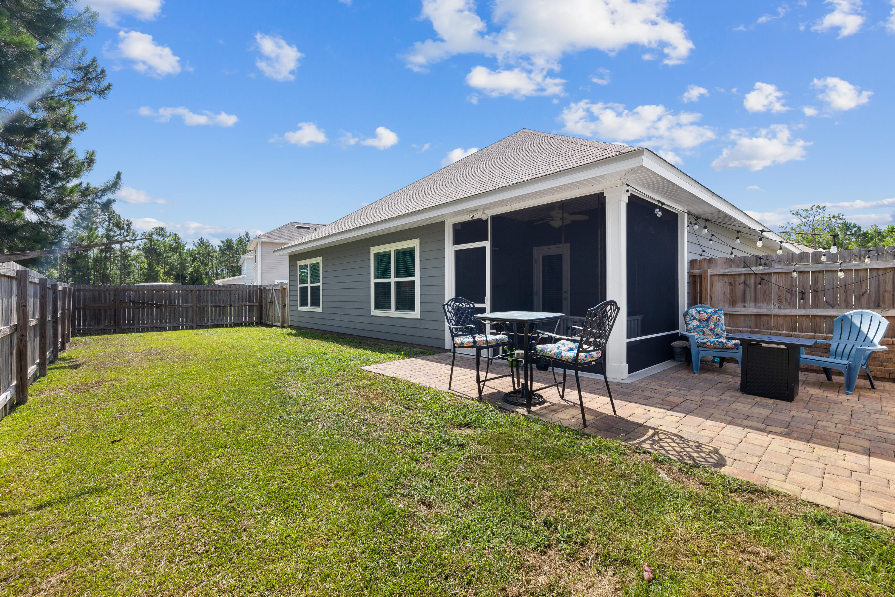 Fenced backyard with a screened porch, brick patio, outdoor dining set, and lawn.