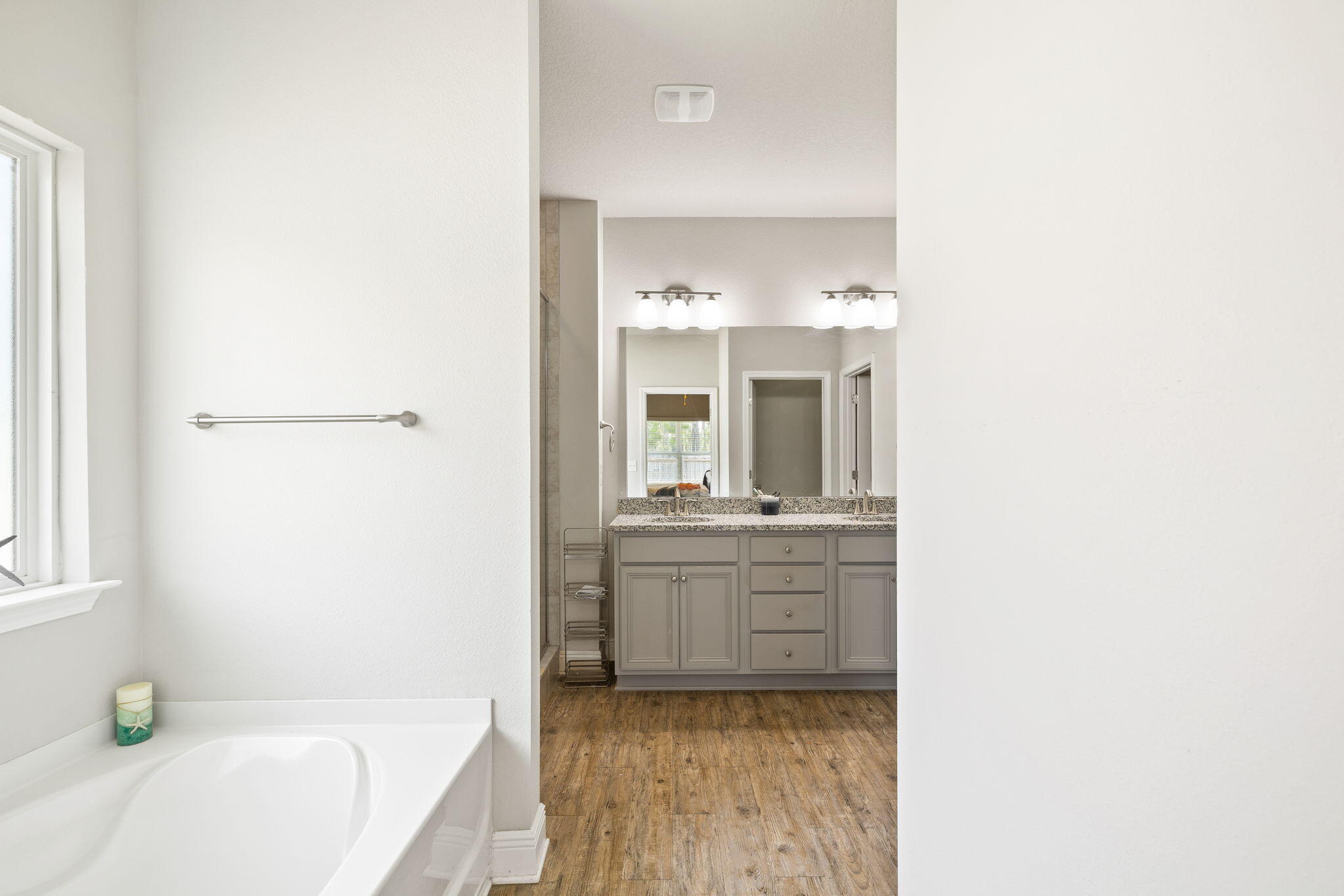Bathroom with a soaking tub beside a window and a double-sink vanity with gray cabinets.