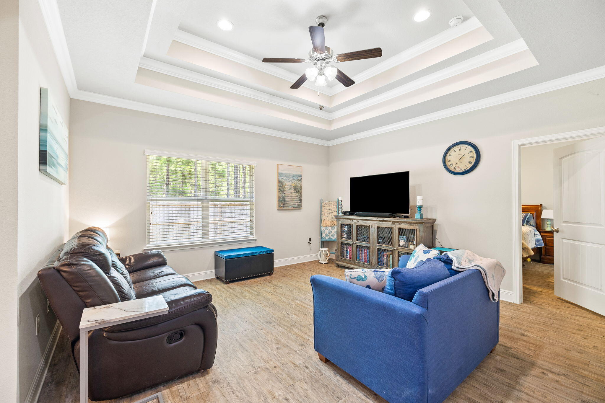Living room with a tray ceiling, ceiling fan, blue sofa, and television cabinet.