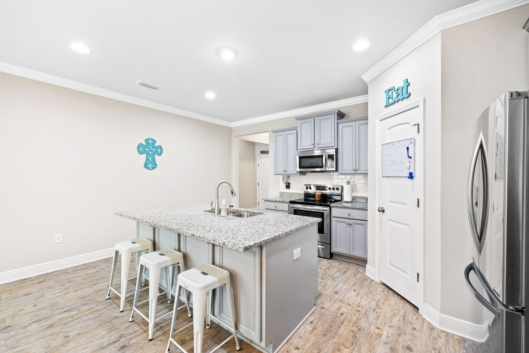 Kitchen with a granite island and three stools, gray cabinets, and stainless steel appliances.