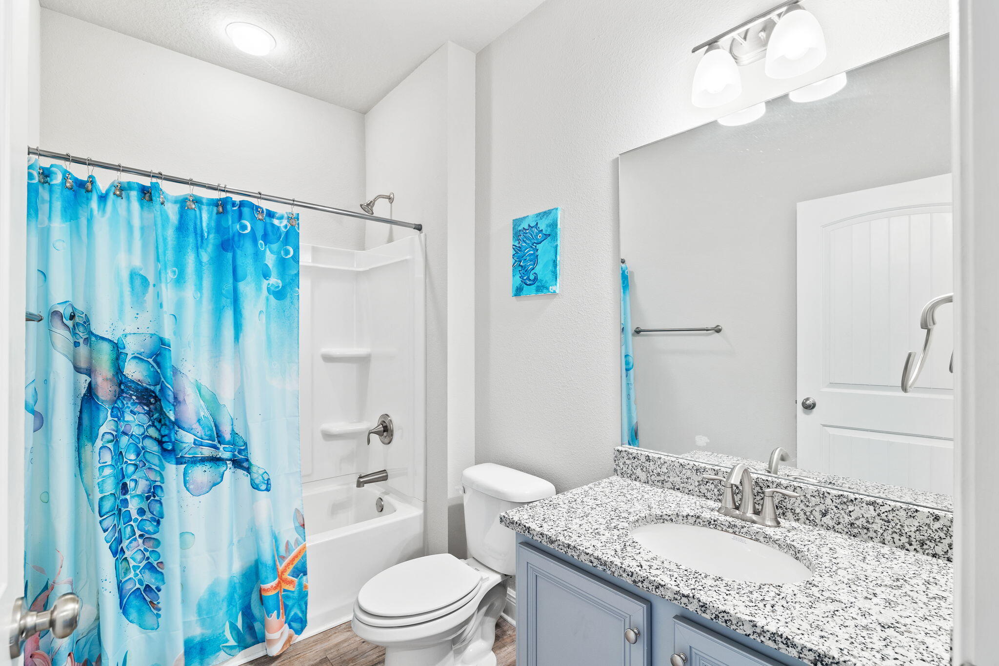 Bathroom with a blue sea turtle shower curtain and granite-topped blue vanity.