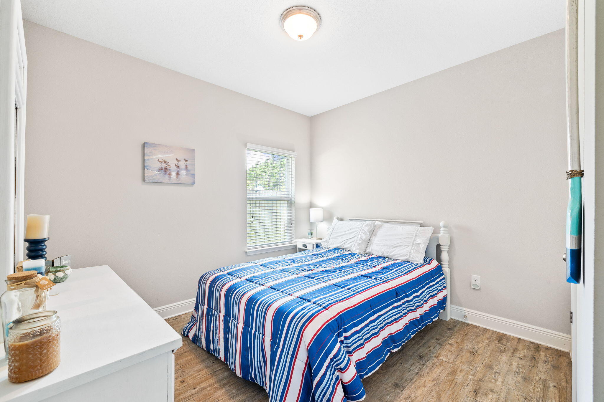 Bedroom with blue, white, and red striped bedding and wood-look flooring
