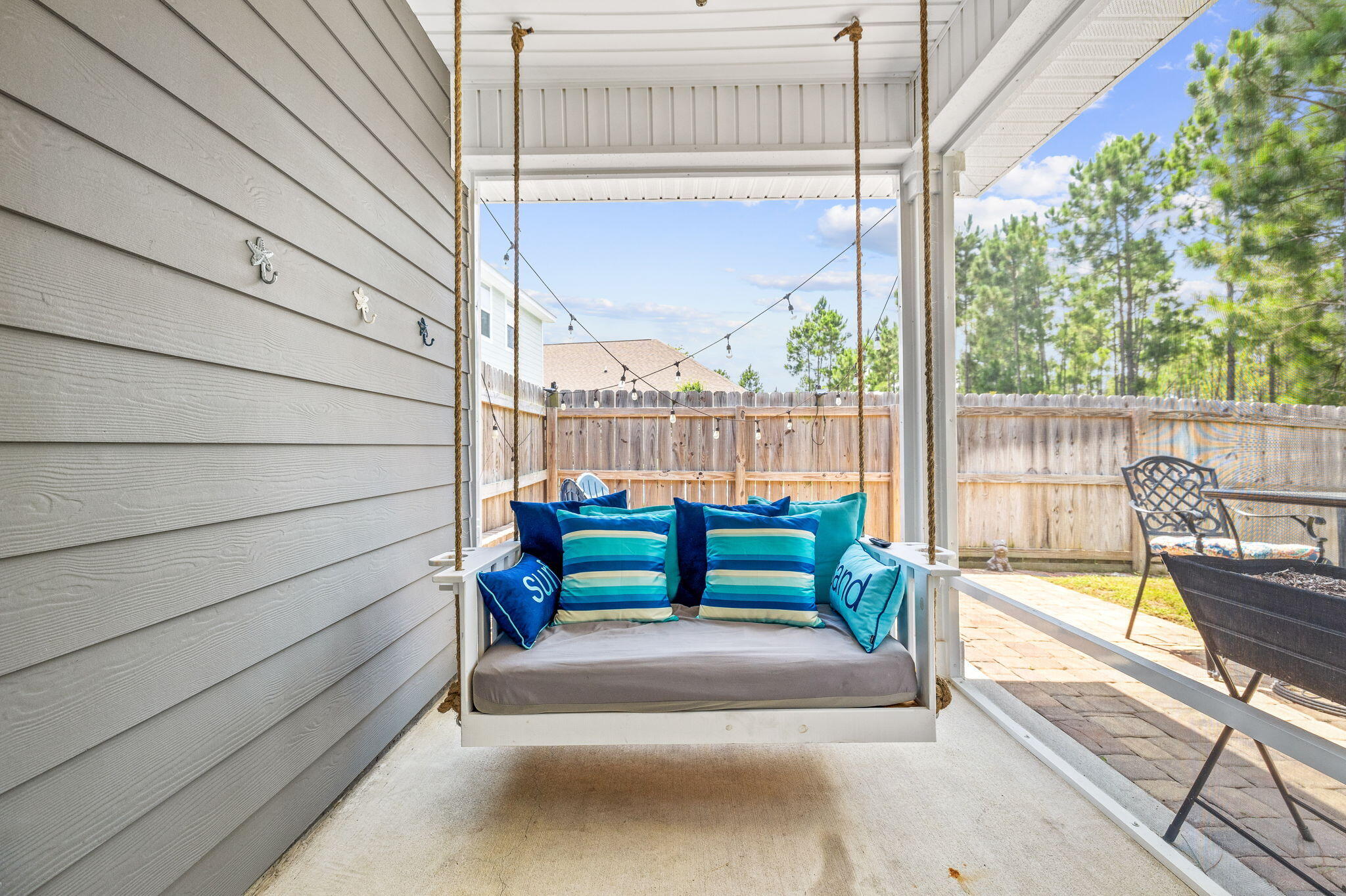 Covered patio with a hanging swing, blue striped cushions, and a fenced backyard.