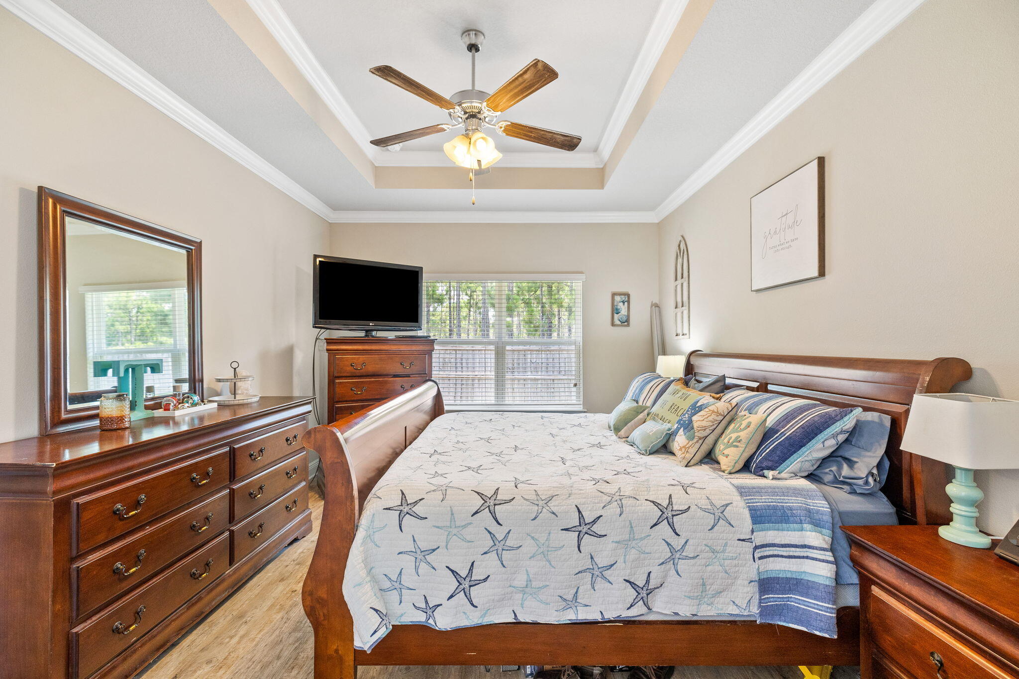 Bedroom with a wooden bed, starfish-patterned quilt, matching dressers, and ceiling fan.