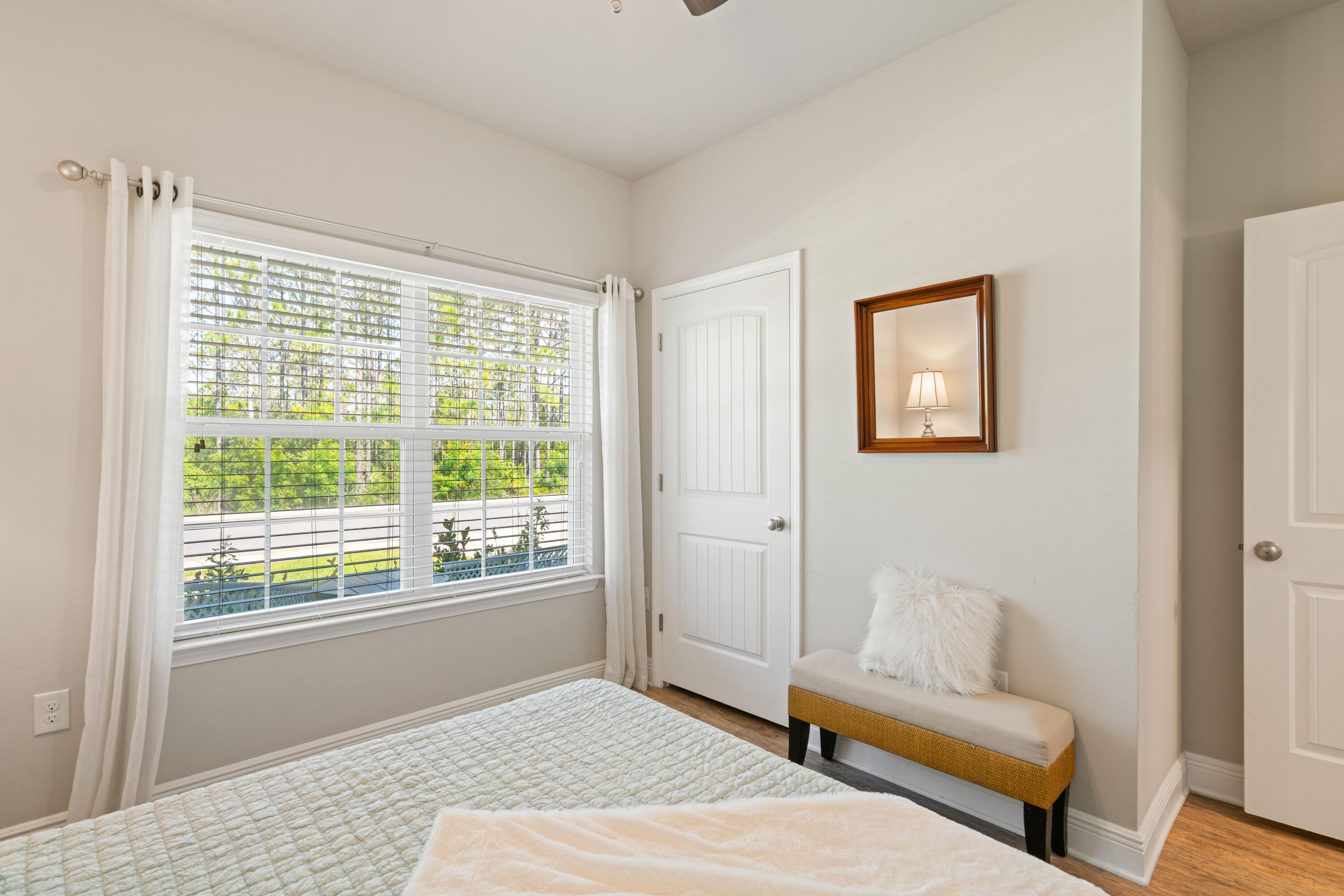 Bedroom with a large tree-facing window, quilted bed, and cushioned bench.