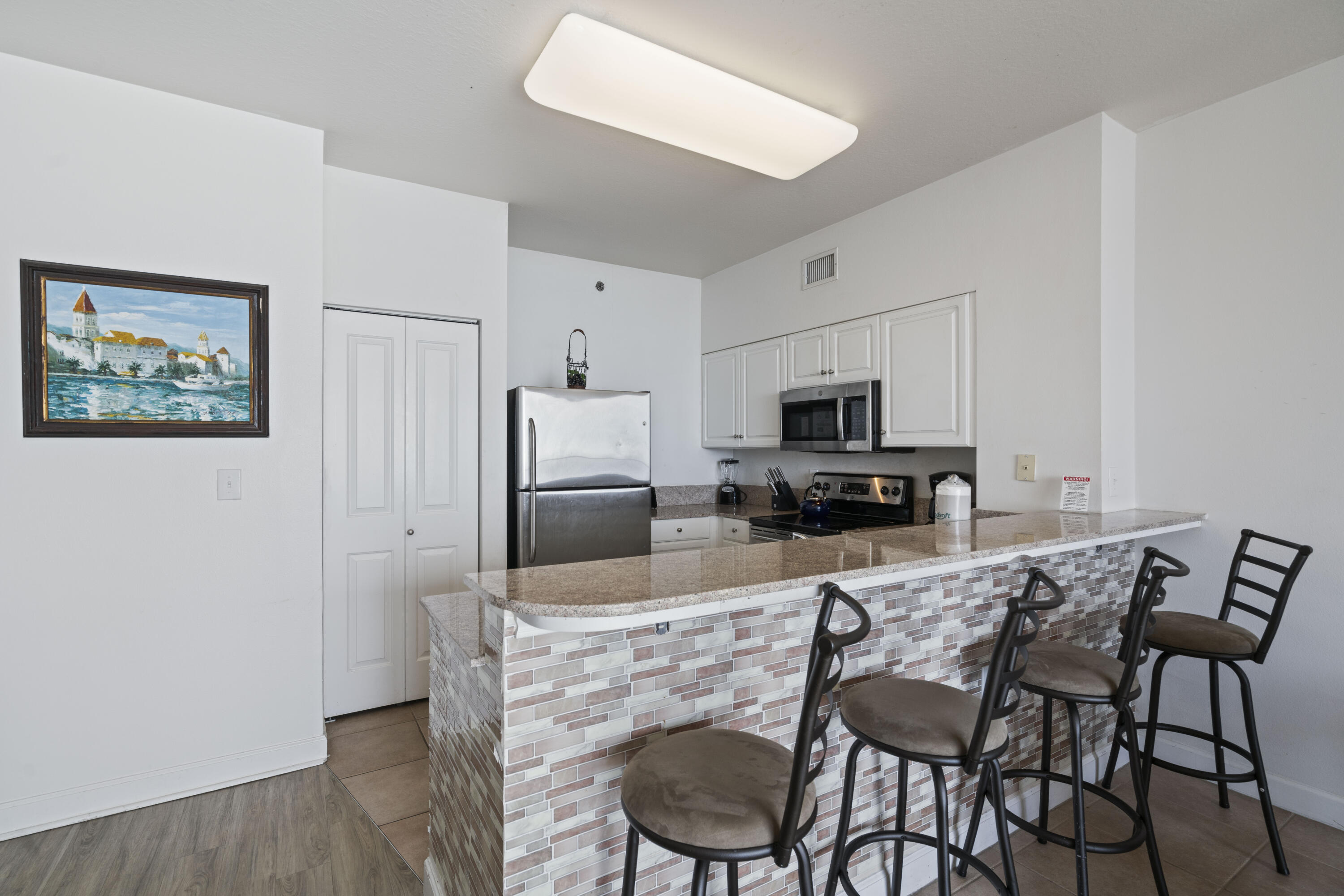 Condo kitchen with stainless steel appliances and a tiled breakfast bar lined with four stools.