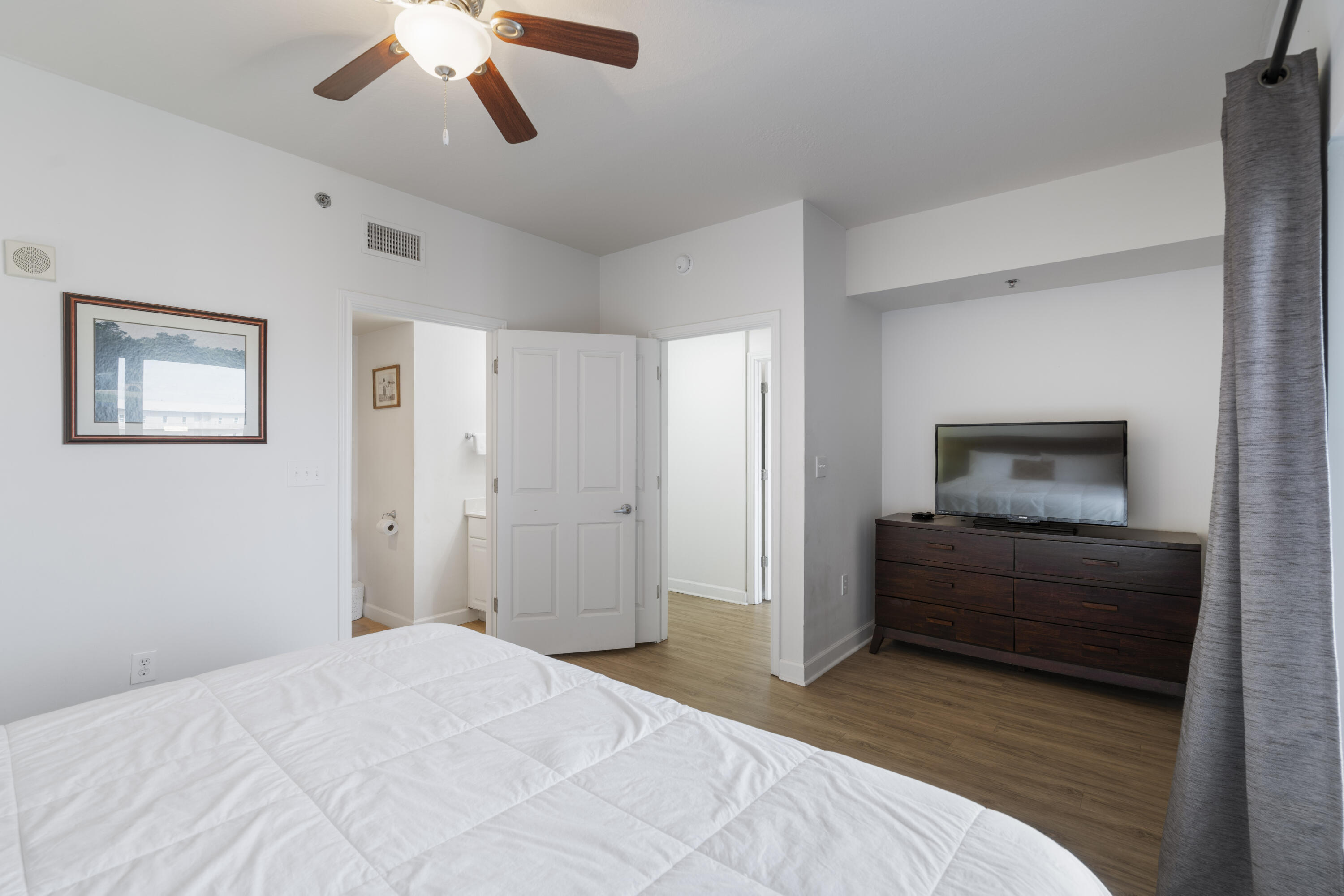 Bedroom with a white bed, ceiling fan, and television on a dark wood dresser.
