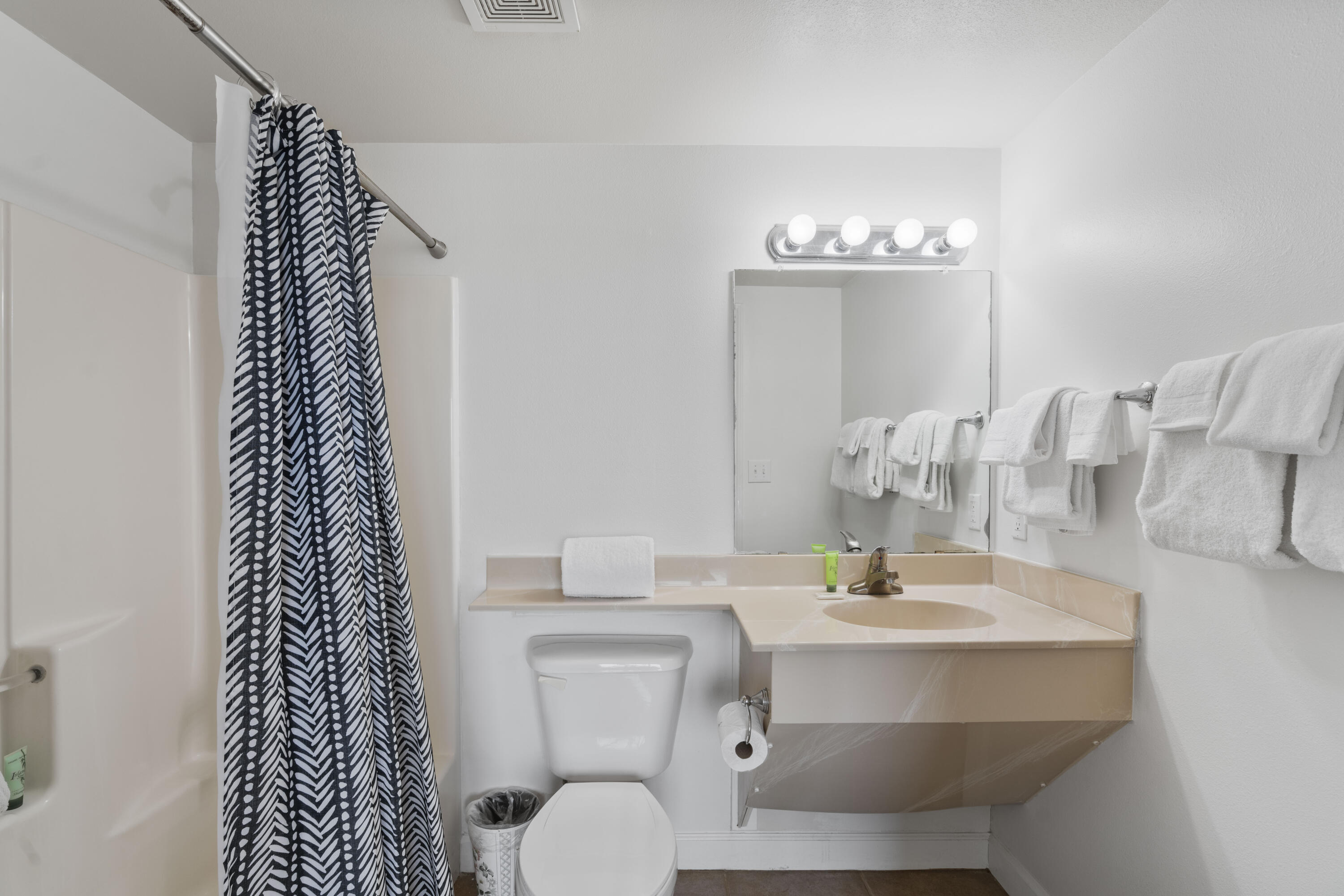 Bathroom with patterned shower curtain, toilet, and beige sink counter beneath a large mirror.