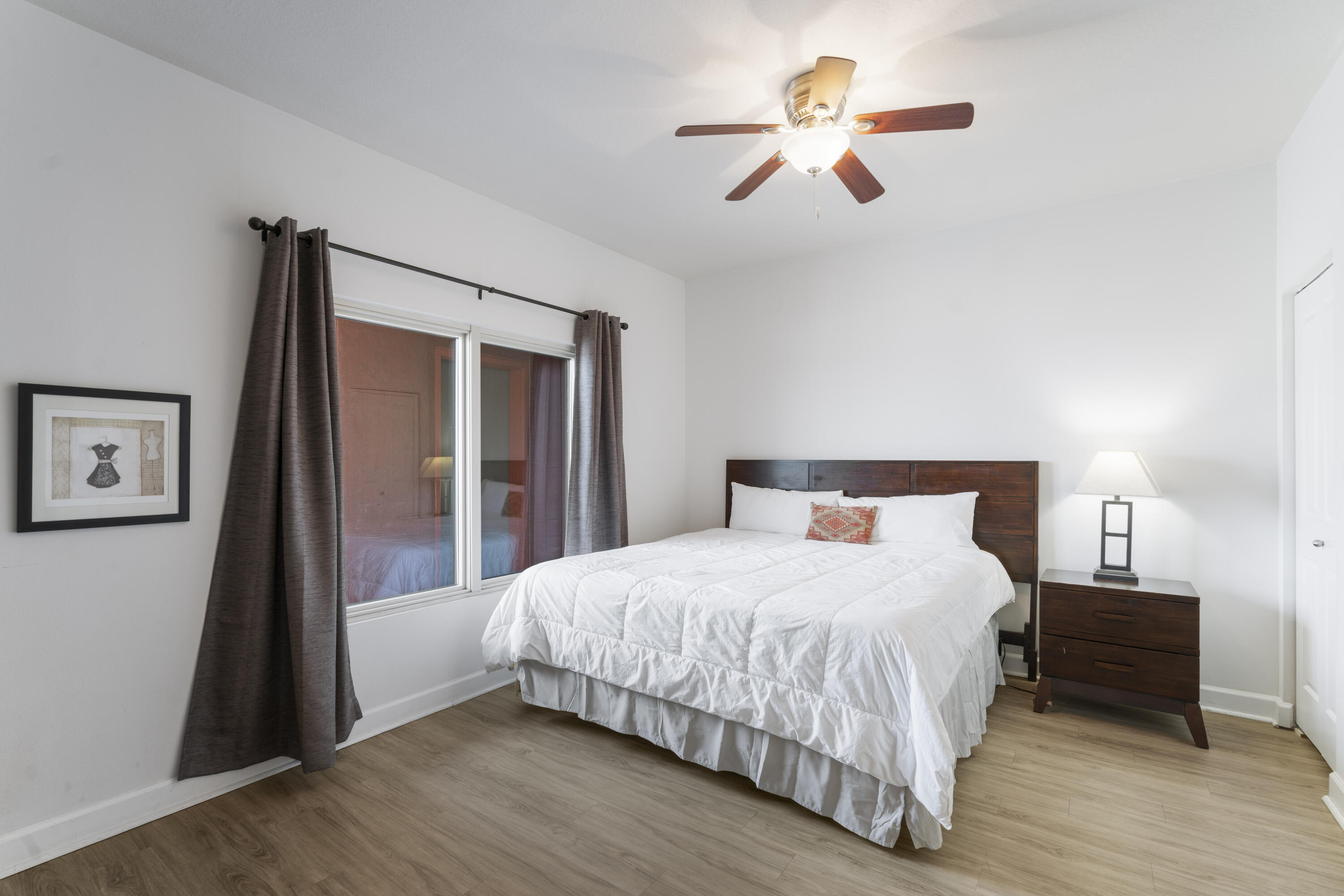 Bedroom with a white-covered king bed, dark wood headboard, gray curtains, and ceiling fan.