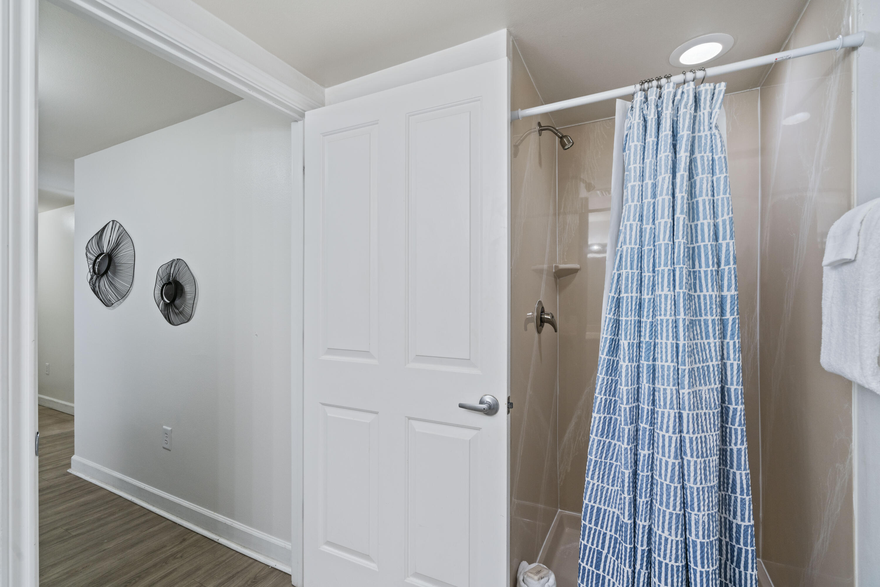 Bathroom shower with tan tile and a blue-and-white patterned curtain beside a white paneled door.