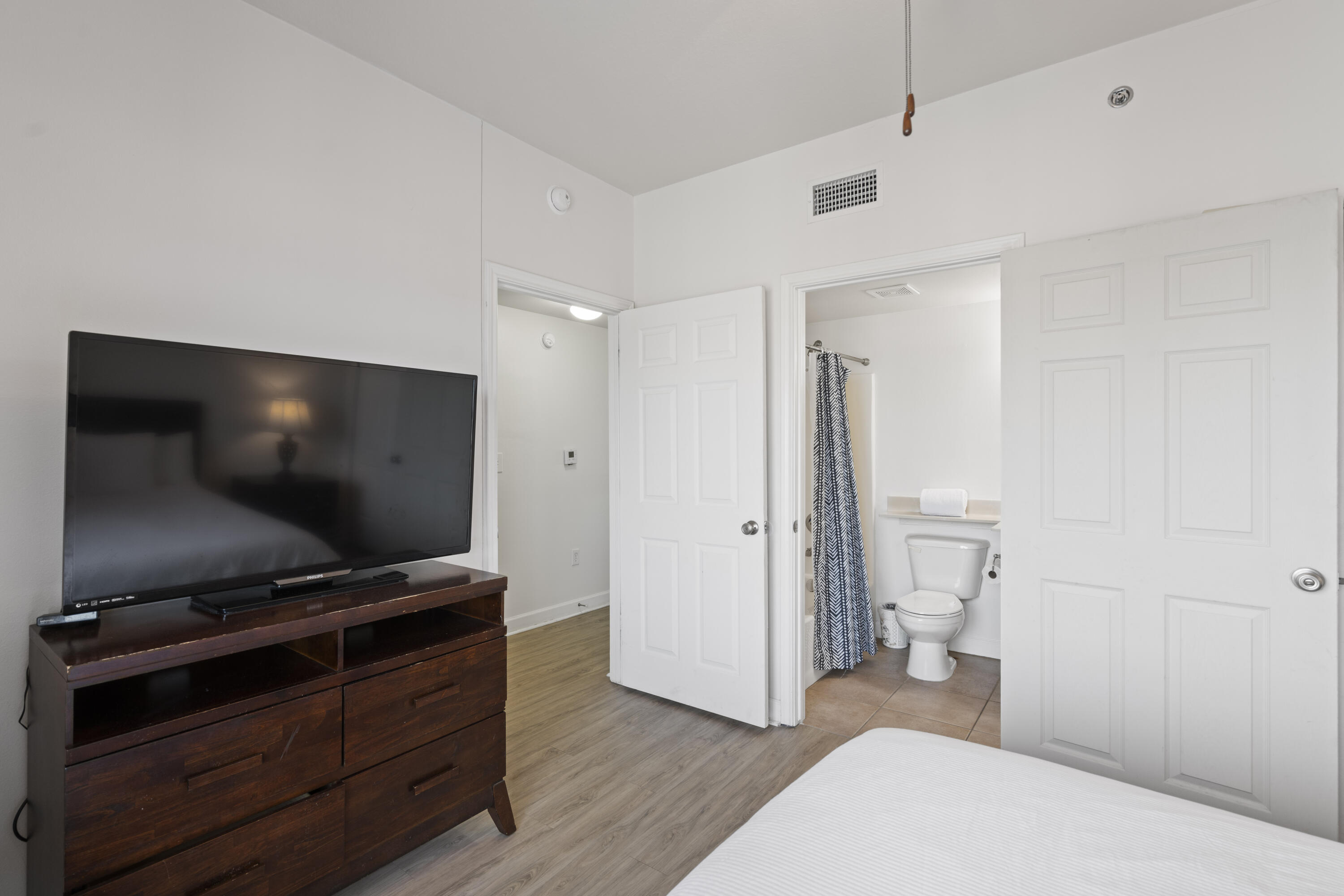 Bedroom with a television and dresser, with an open doorway to a bathroom.