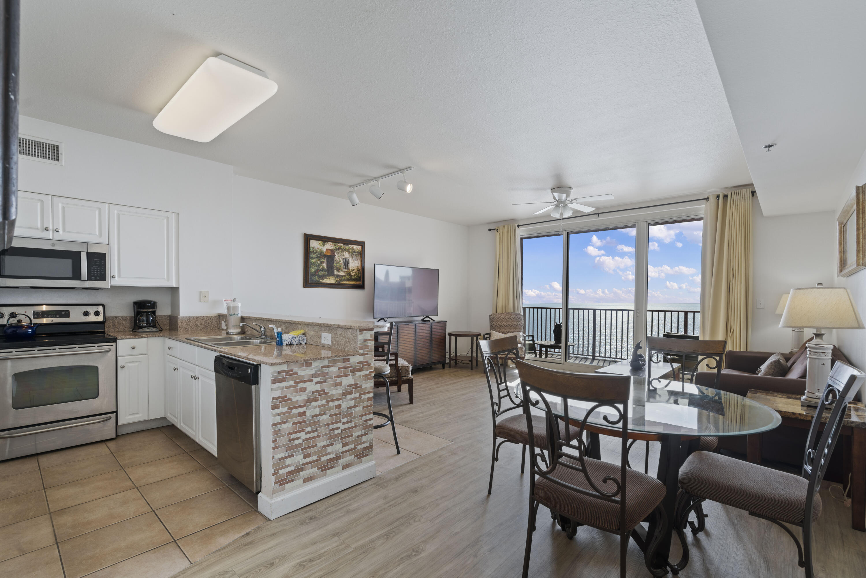 Open-plan condo kitchen and dining area with a brick-front breakfast bar and balcony overlooking the water.