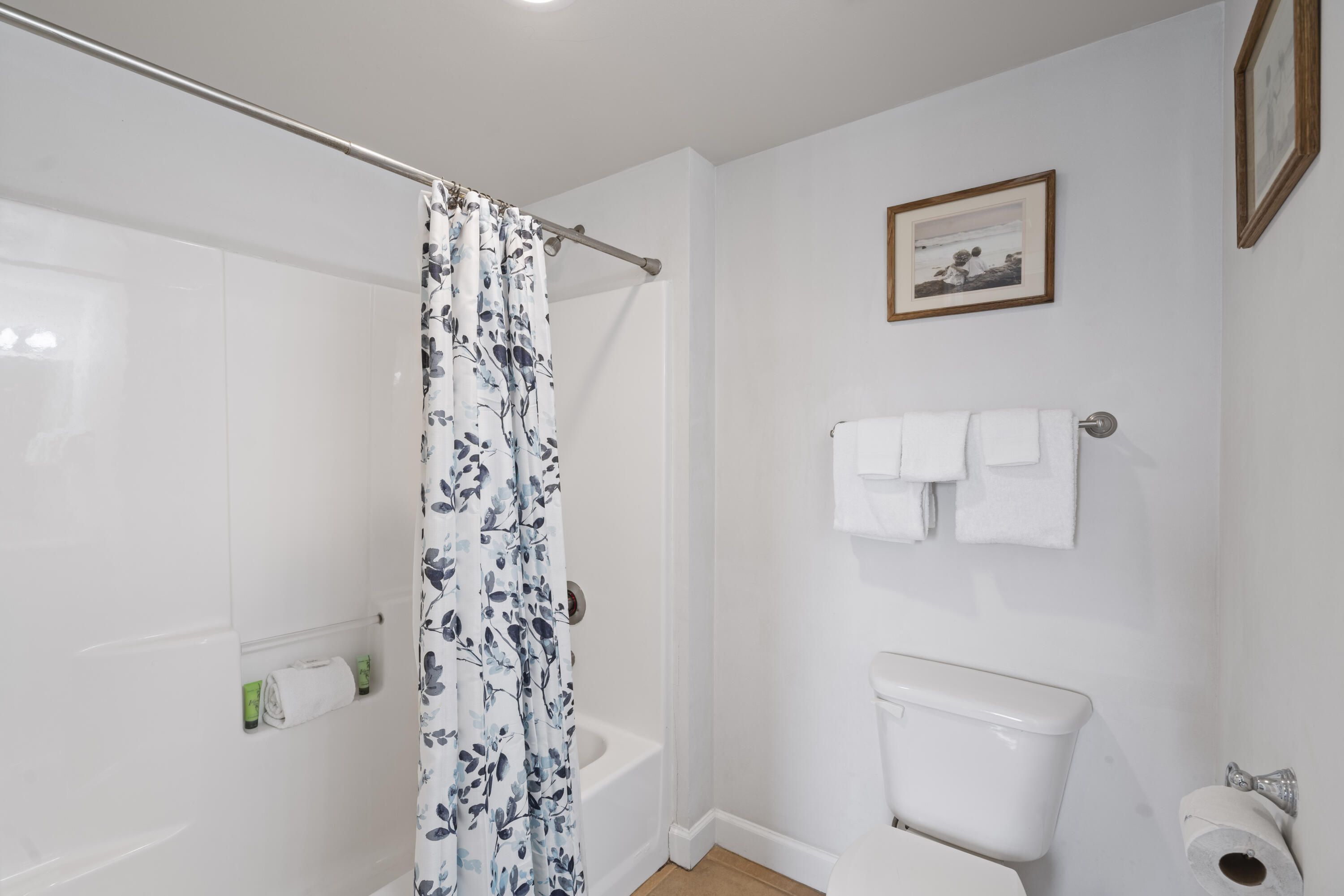 Bathroom with a floral shower curtain, white bathtub, toilet, and neatly hung towels.