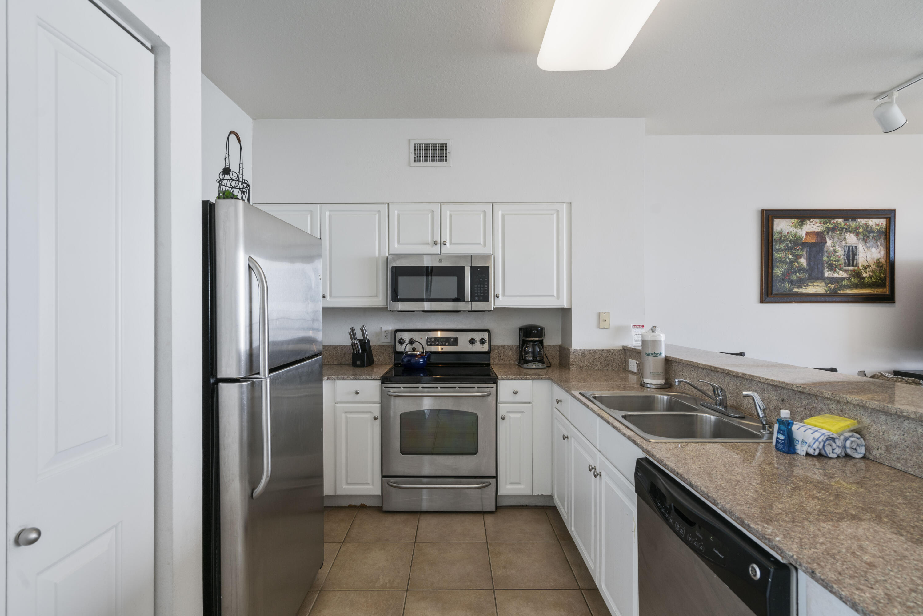 Condo kitchen with white cabinets, stainless steel appliances, and a double-basin sink.