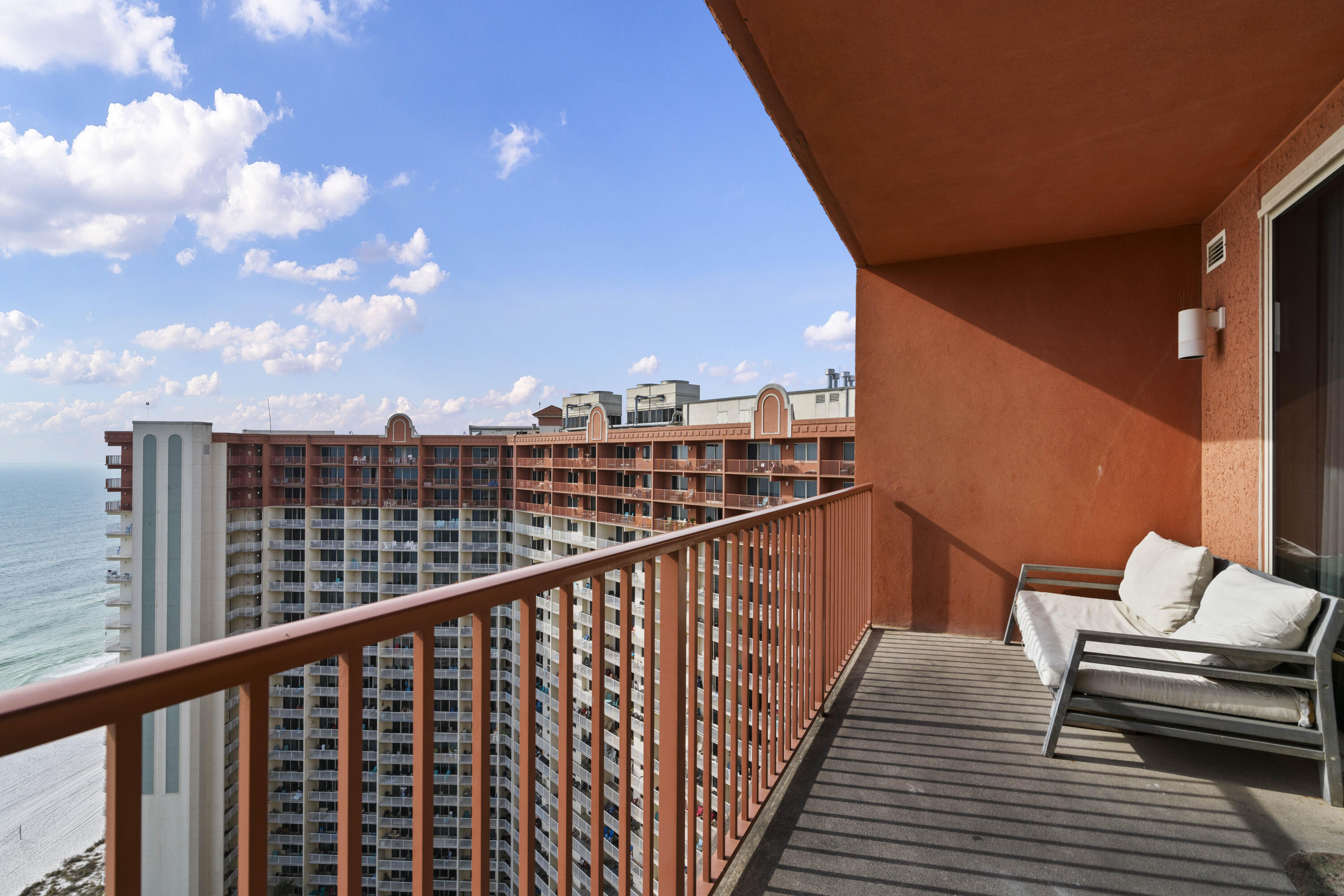Condominium balcony with cushioned seating overlooking the ocean and a neighboring high-rise.