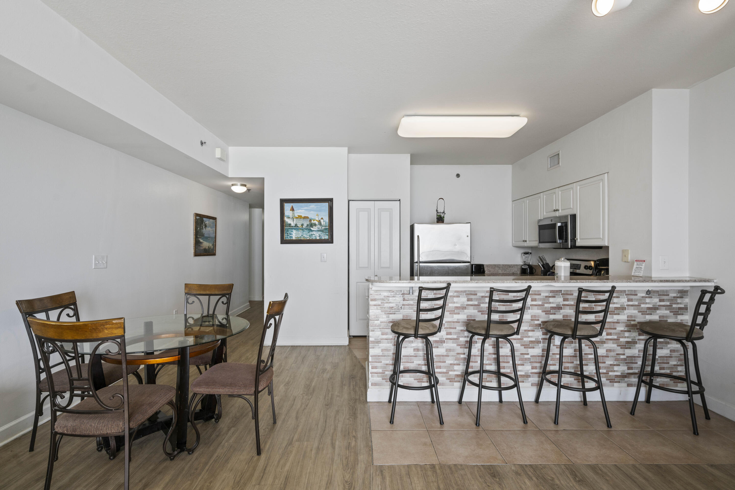 Open-plan kitchen and dining area with a tiled breakfast bar, four stools, and stainless steel appliances.