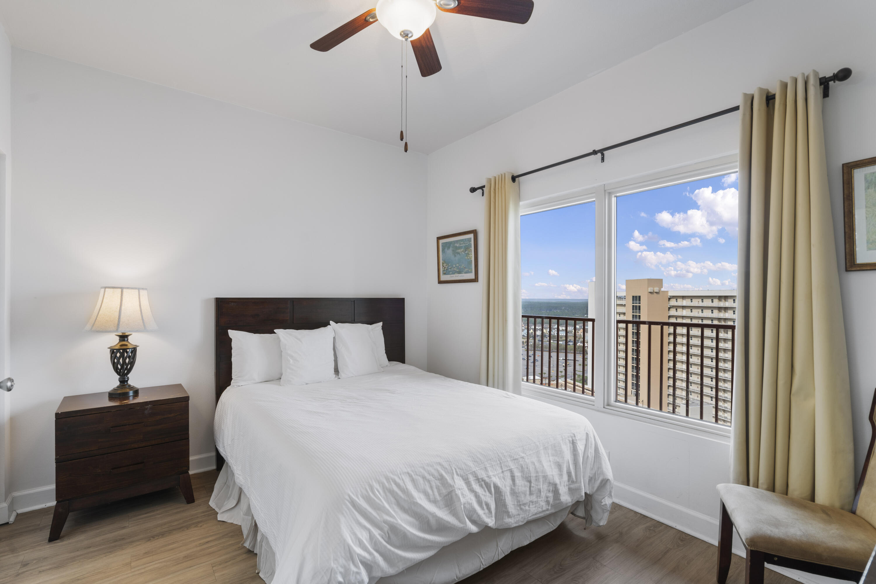 Bedroom with a white bed and large windows overlooking the water and a neighboring high-rise.