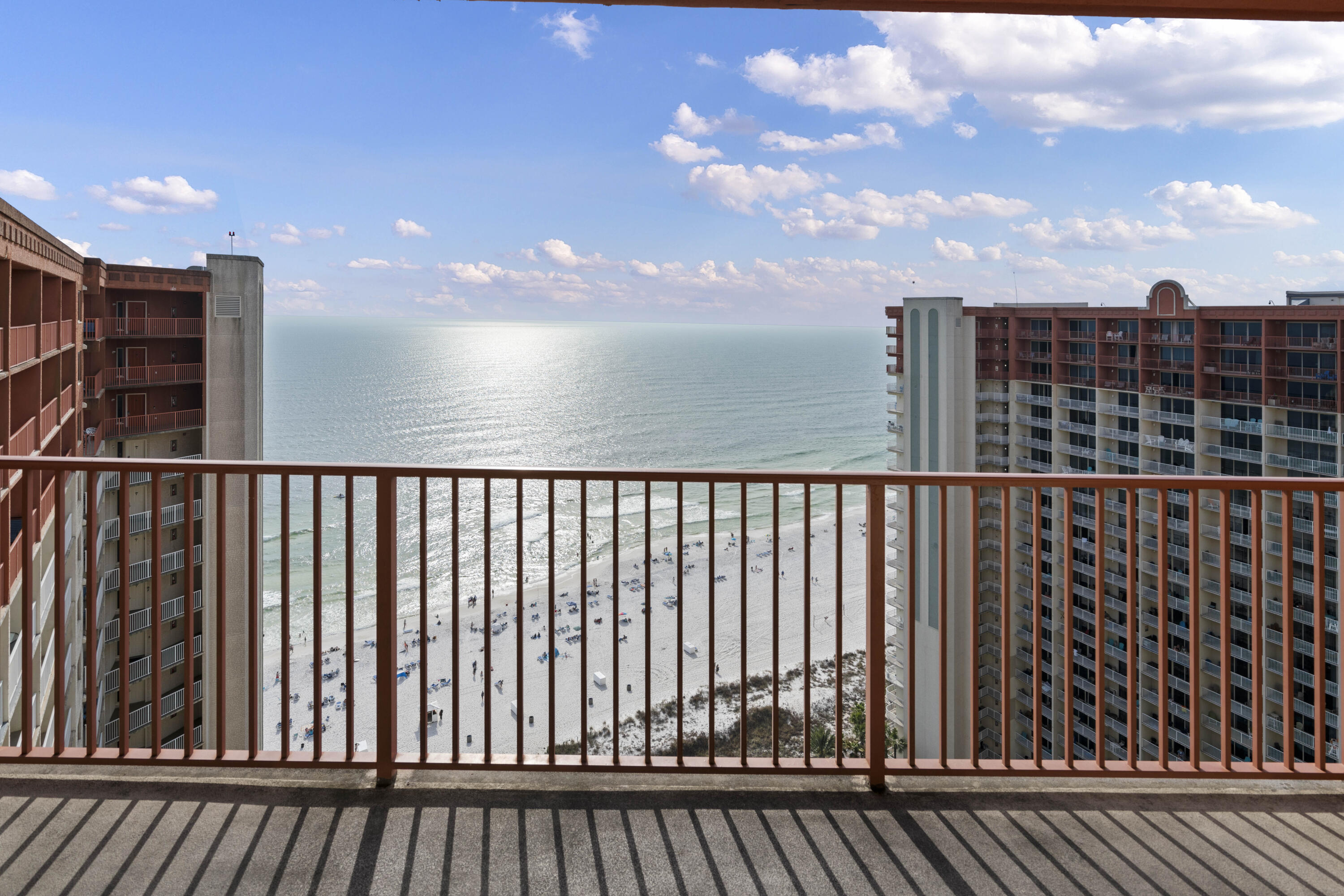 Ocean and beach view from a high-rise balcony, framed by neighboring condominium towers.