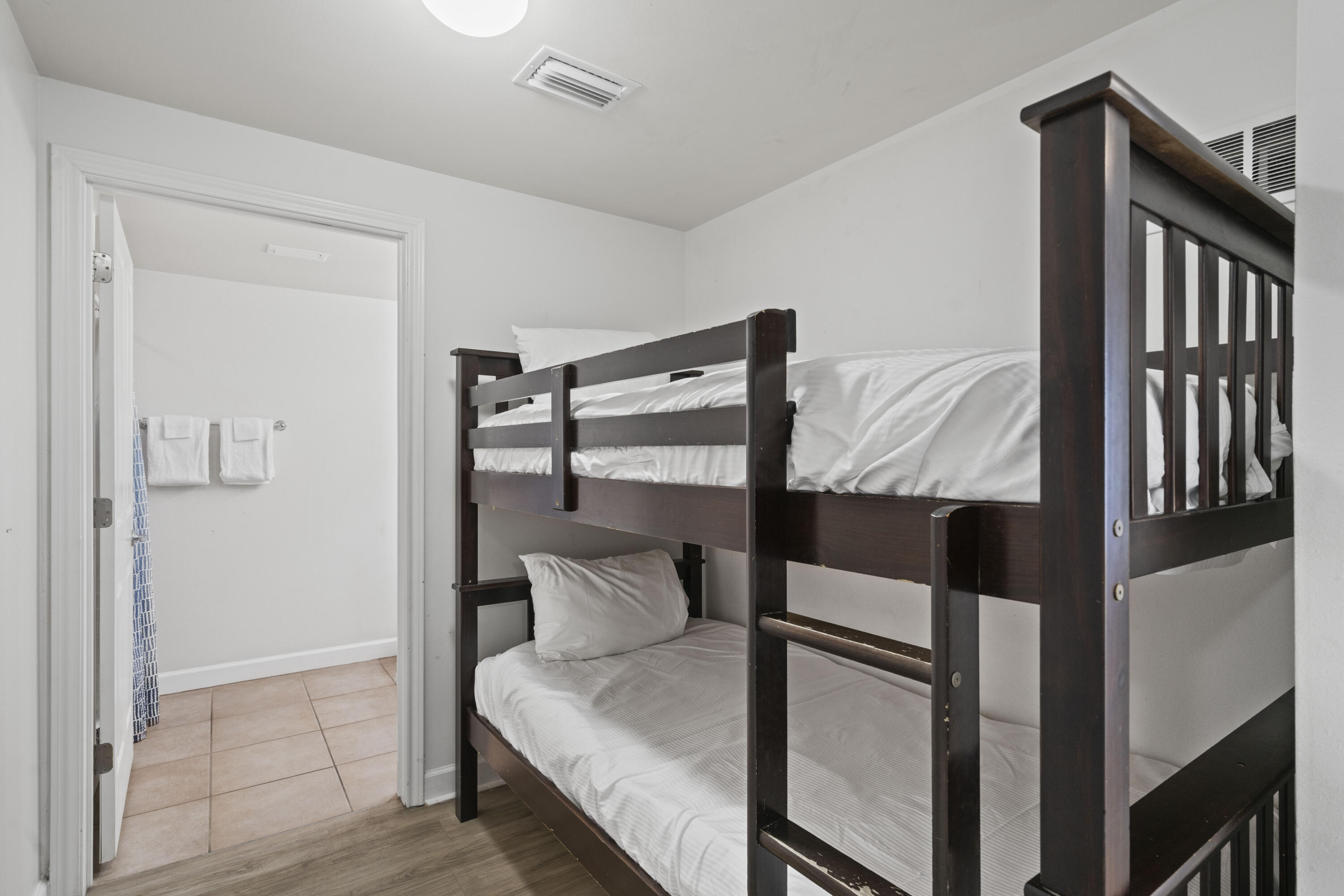 Bedroom with a dark wood bunk bed and an open doorway to a tiled bathroom.