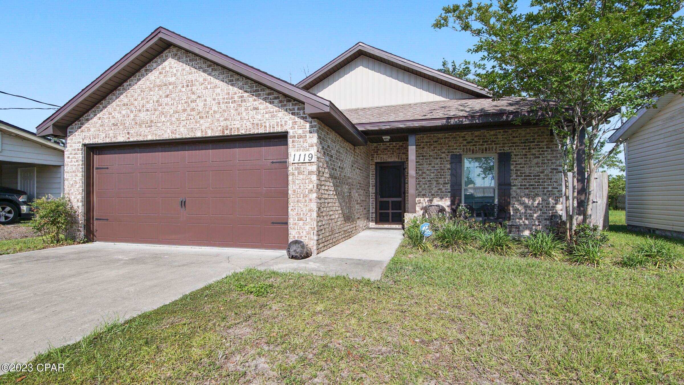 Brick house with a brown double garage door, covered porch, and front lawn.
