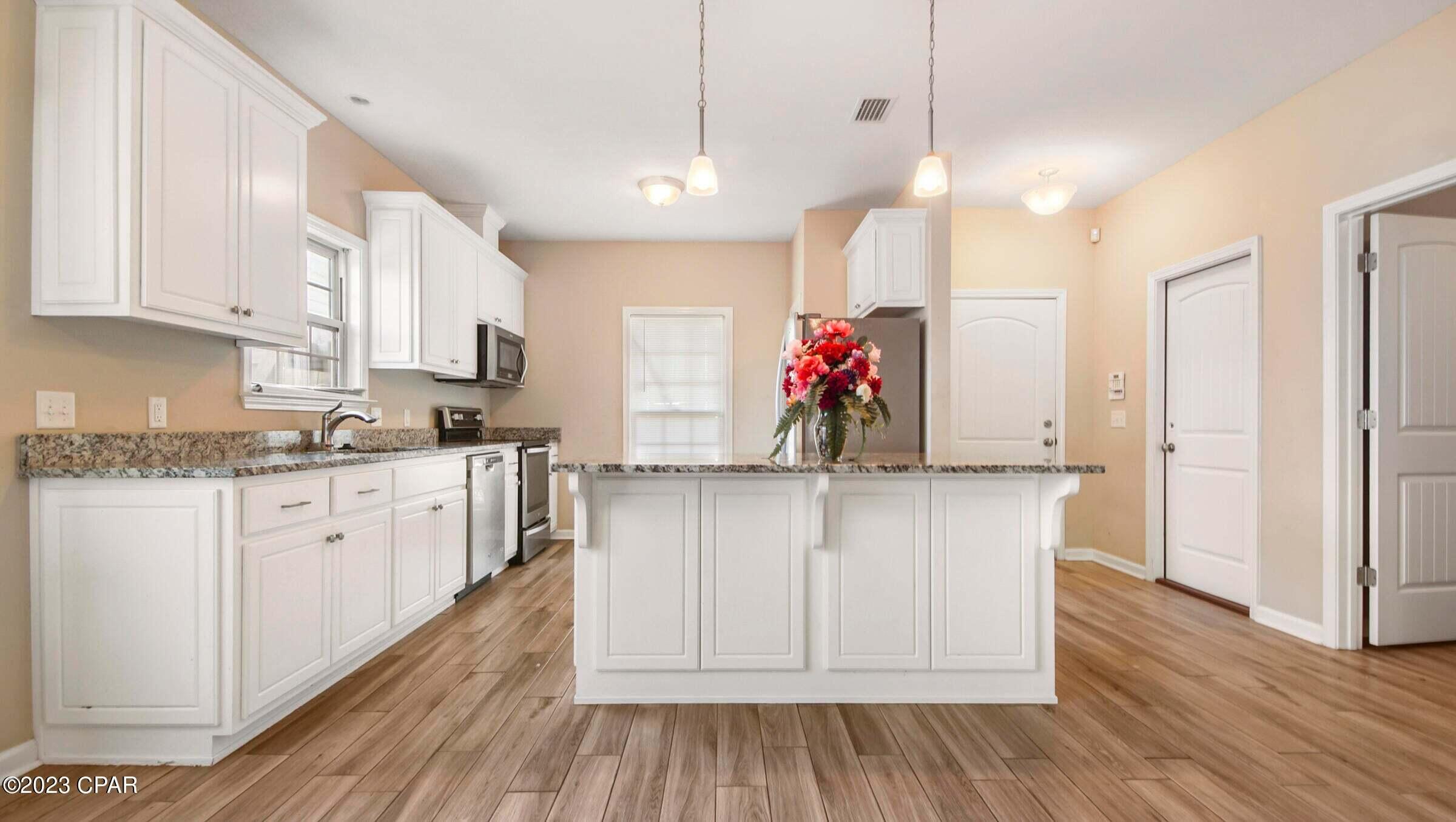 Kitchen with white cabinets, granite countertops, stainless steel appliances, and a central island.