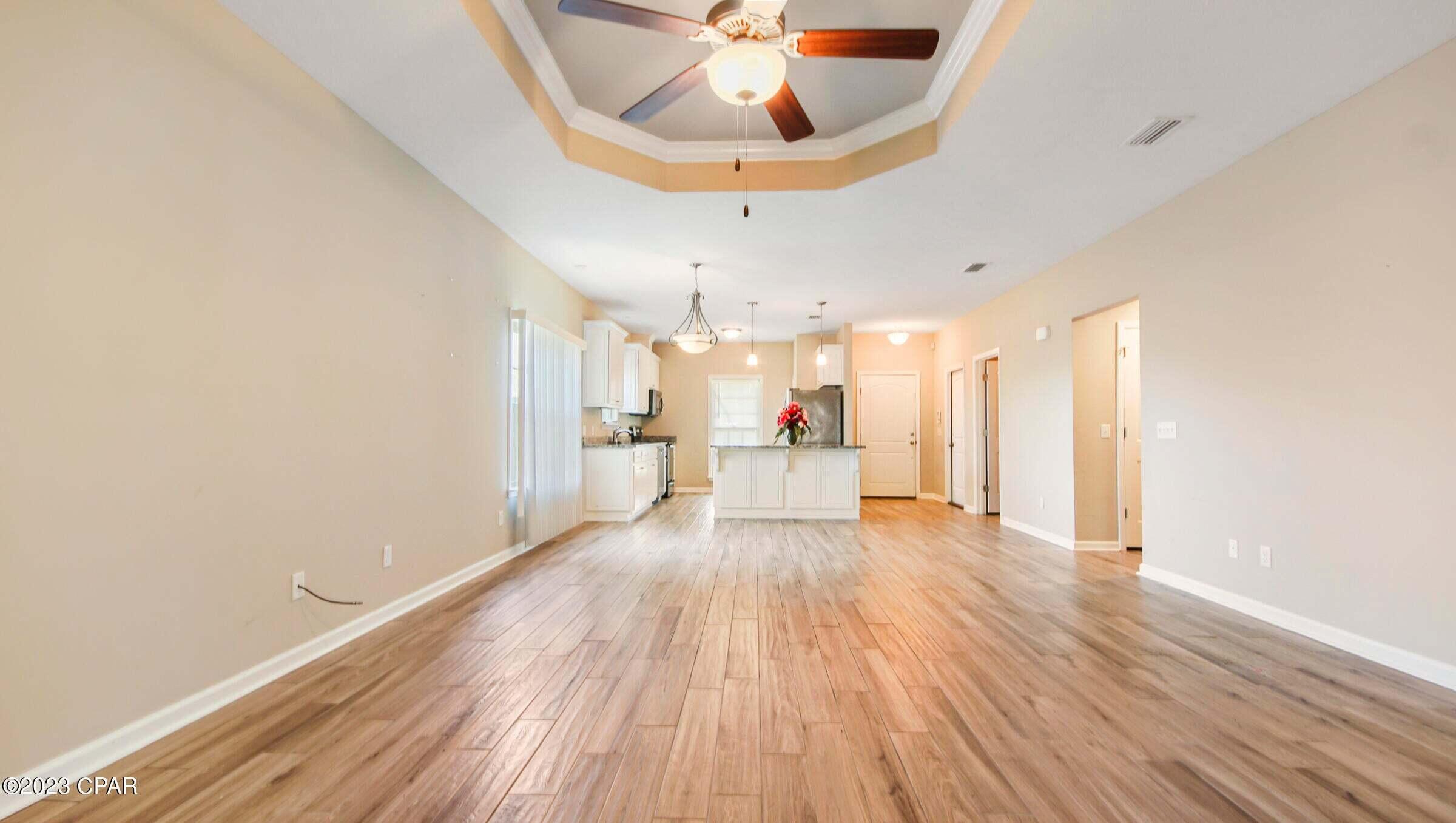 Empty open-plan living area with wood-look tile flooring, tray ceiling, and kitchen island beyond.