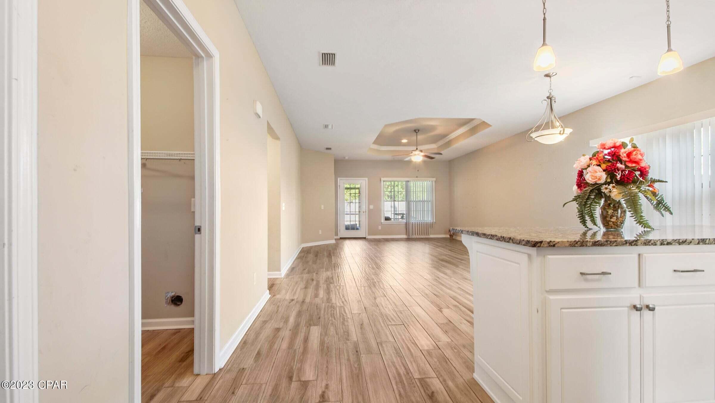 Open living and dining area with a white kitchen island, wood-look floors, and a tray ceiling.