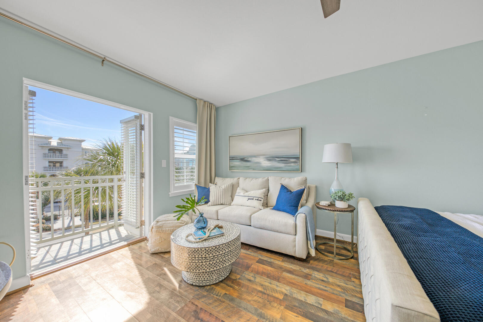 Bedroom with a blue-covered bed, sitting area, and sunny balcony doors.