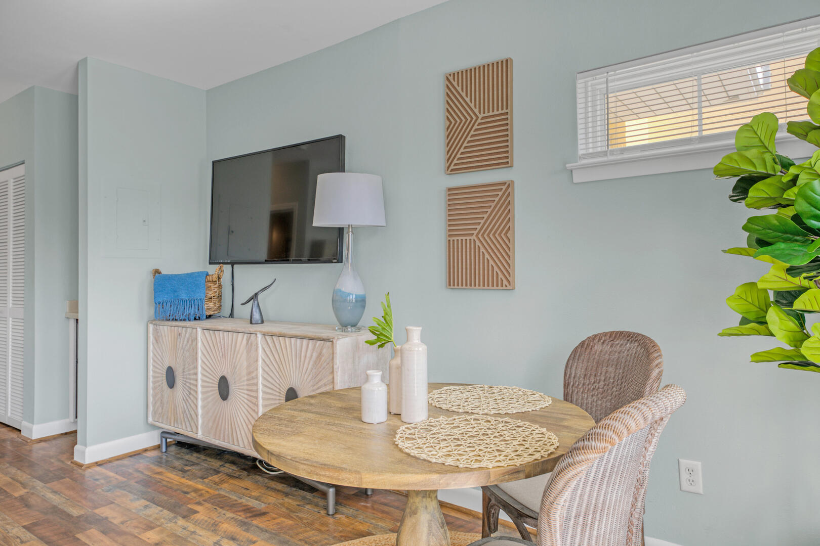 Condo dining area with a round wood table, woven chairs, a sideboard, and a wall-mounted TV.