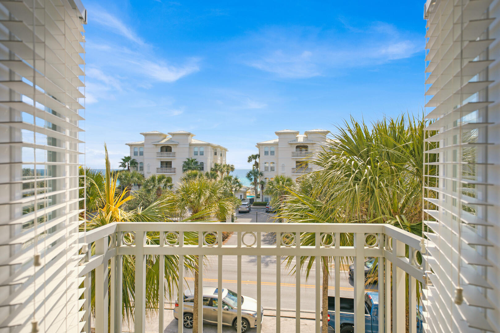 Condo balcony view framed by palms, with neighboring buildings and a glimpse of Gulf water.