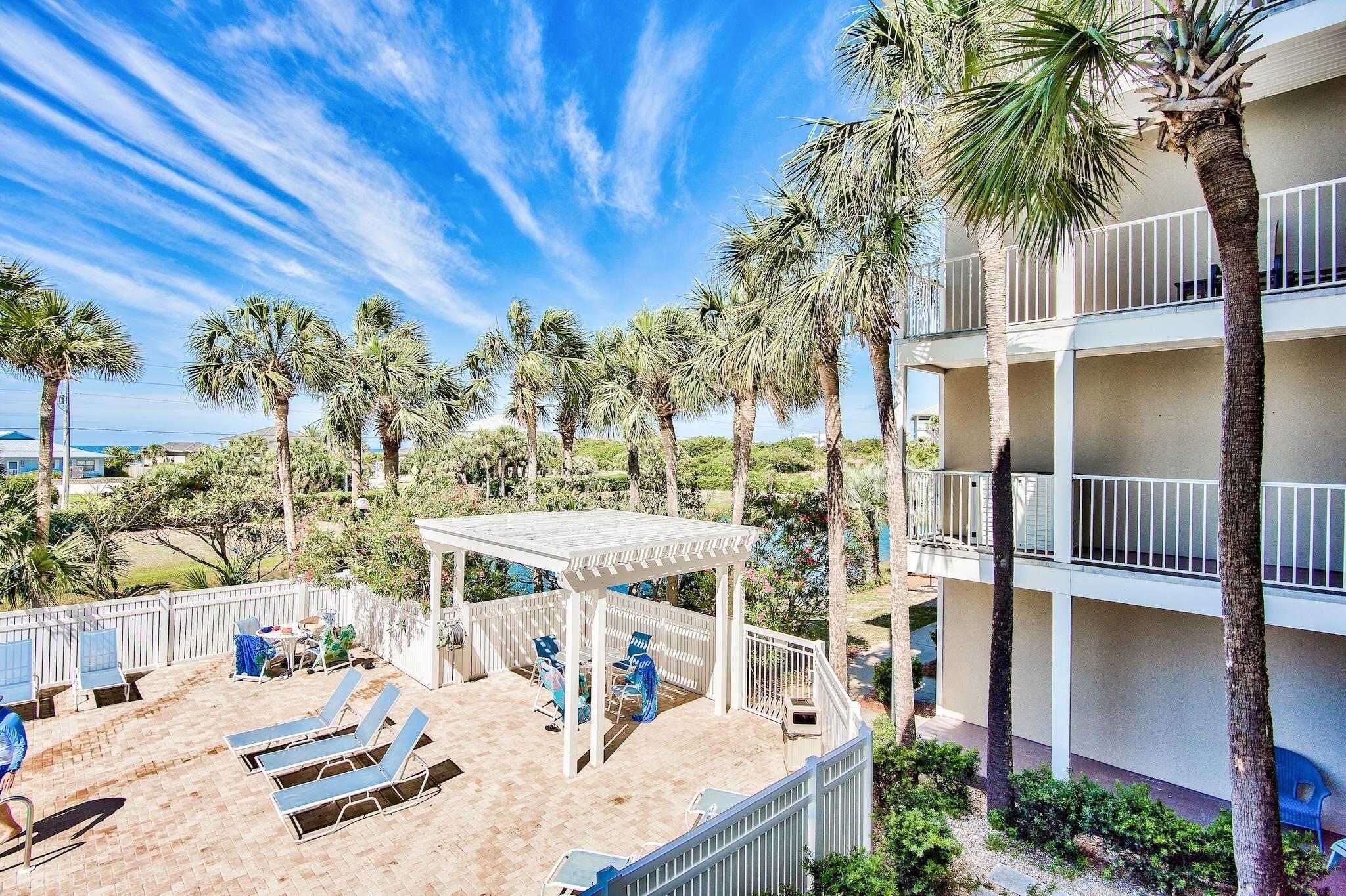 Condominium courtyard with palm trees, a paved pool deck, lounge chairs, and a covered seating area.