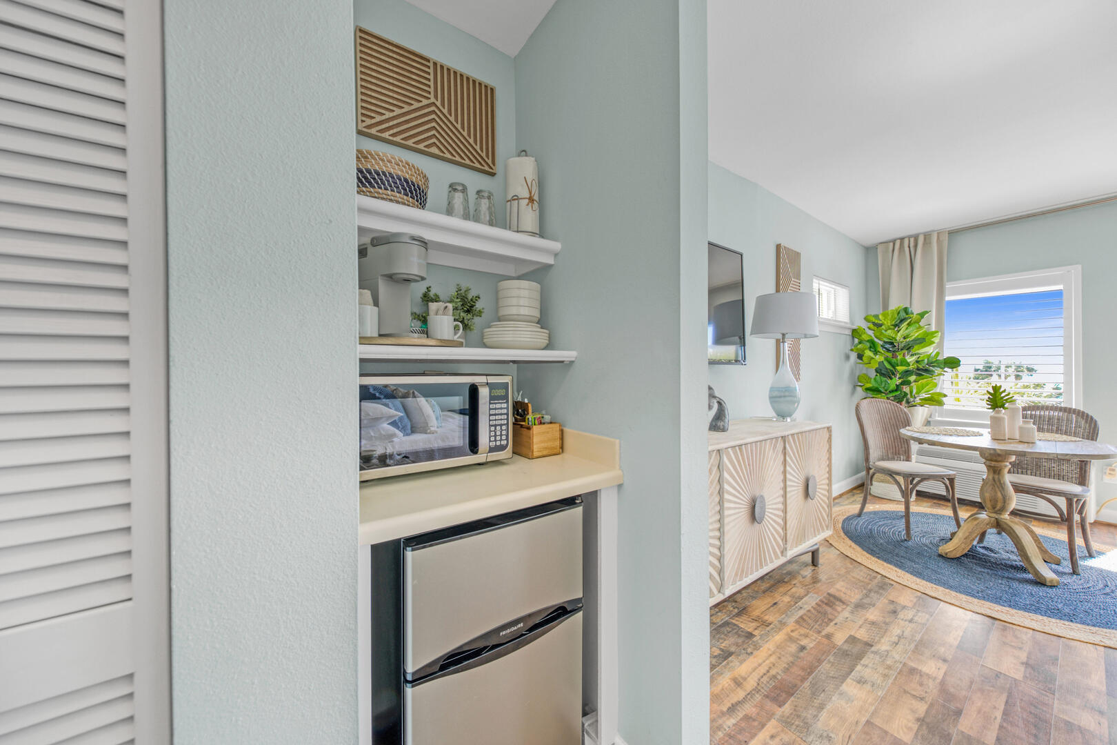 Furnished condo kitchenette and dining area with wicker chairs and large windows.