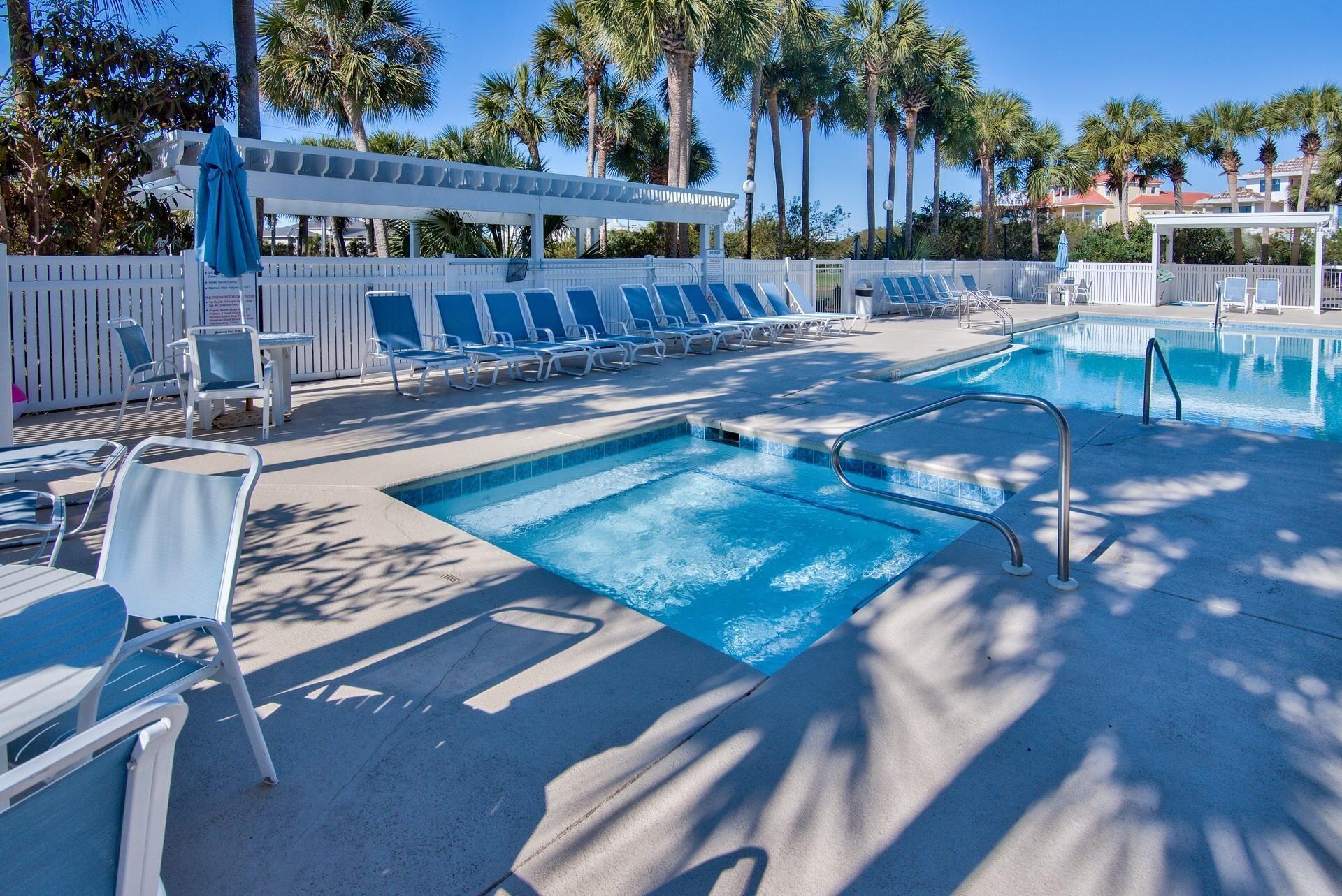 Outdoor pool with a shallow section, blue loungers, white fencing, and palm trees.