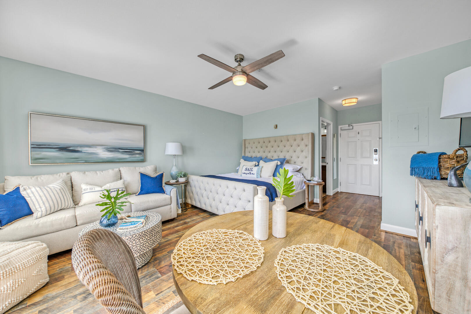 Furnished studio bedroom and living area with a tufted bed, cream sofa, and blue accents.