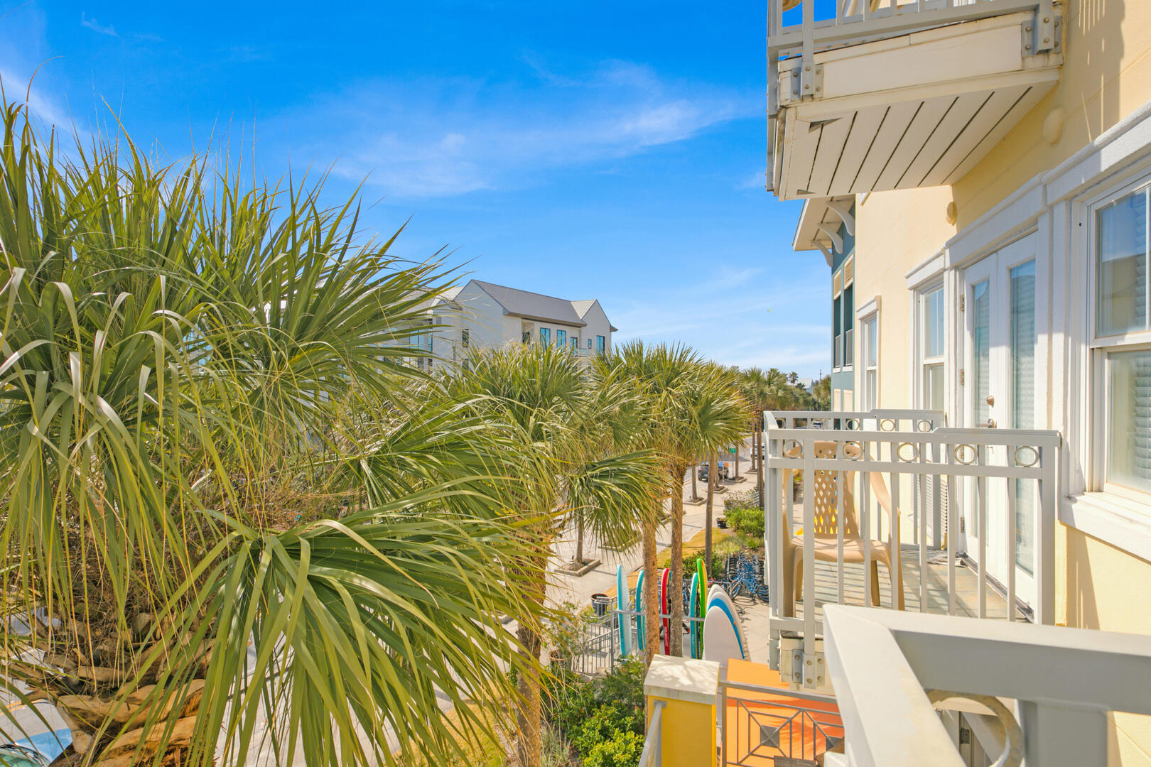 Condo balcony overlooking palm landscaping, a walkway, and colorful surfboards.