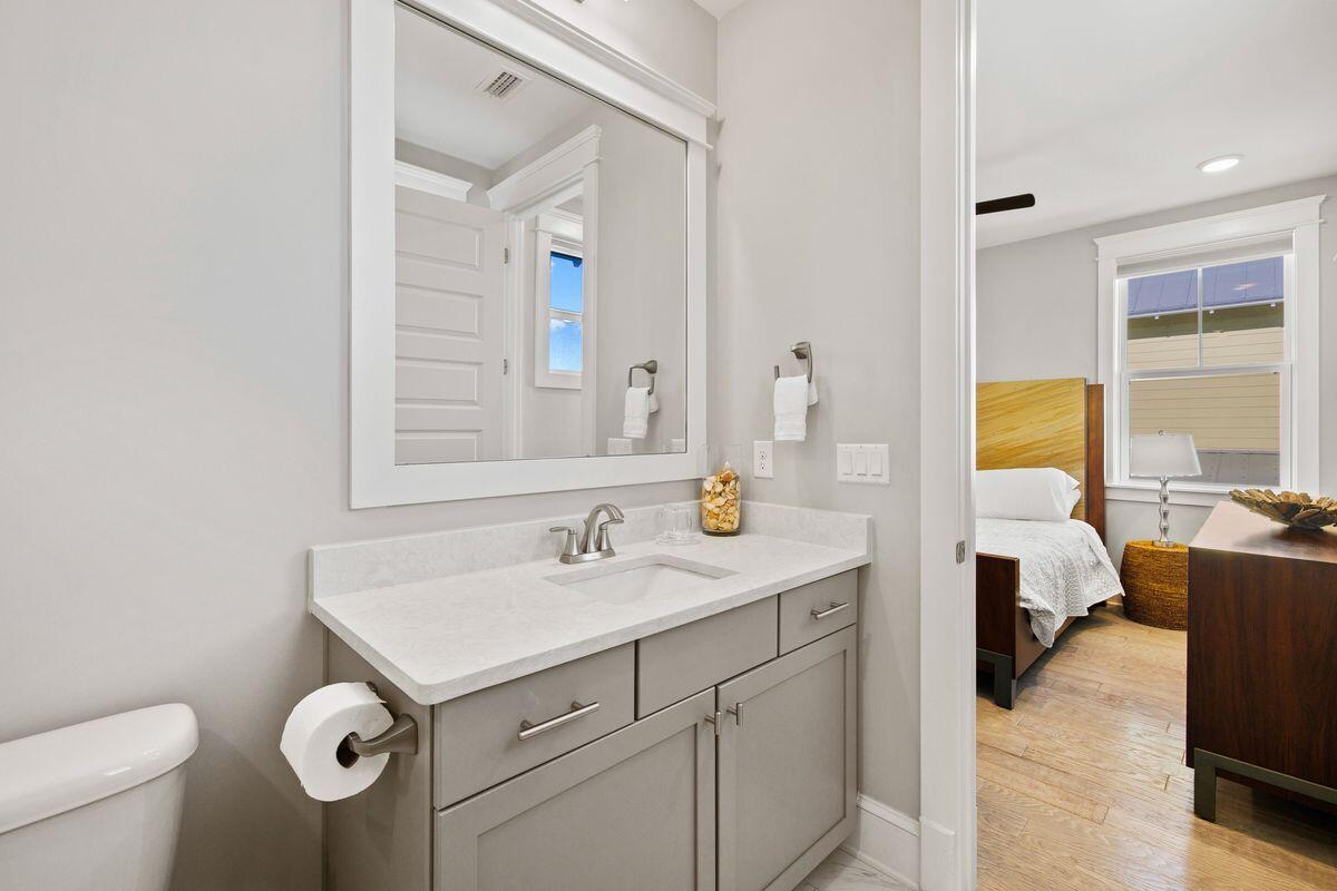 Bathroom vanity with a large mirror; a furnished bedroom is visible through the open doorway.