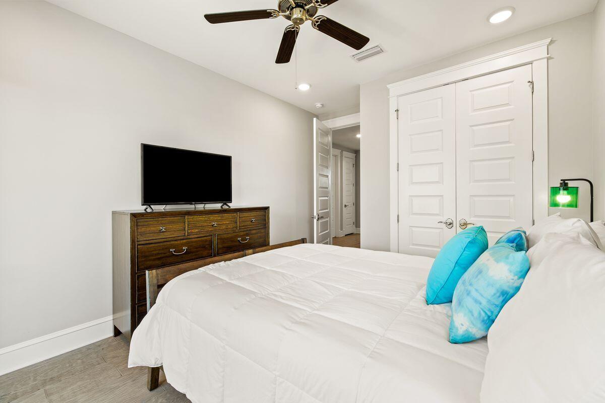 Bedroom with white bedding, turquoise pillows, dark wood dresser, and ceiling fan.