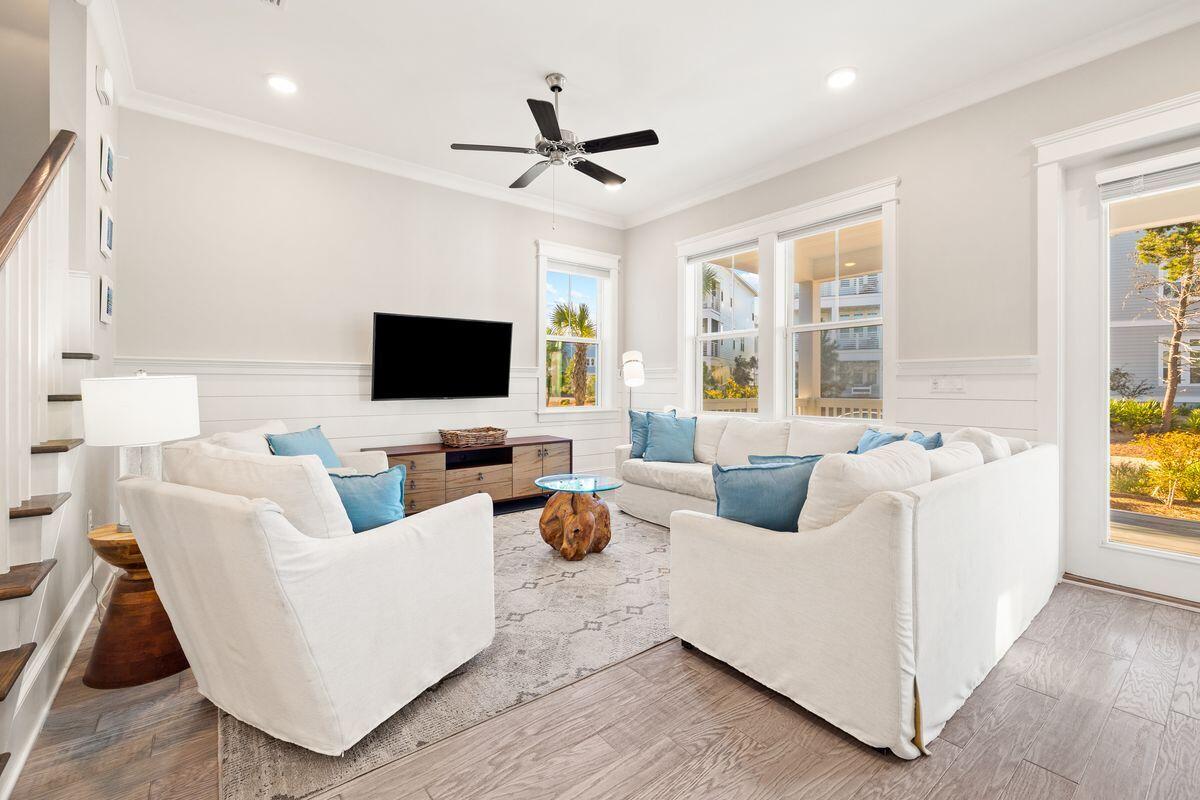 Living room with white sofas, blue pillows, large windows, and a ceiling fan.