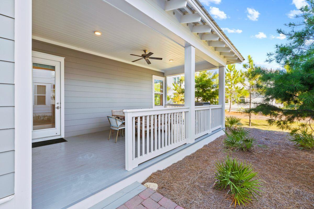 Covered porch with white railings, a ceiling fan, and seating beside a landscaped yard.