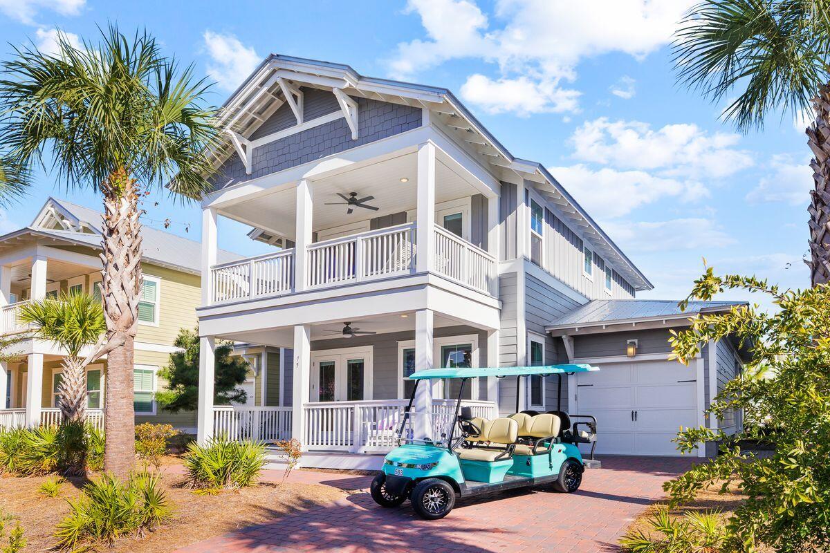 Gray coastal-style home with two covered balconies, an attached garage, and a turquoise golf cart in the driveway.