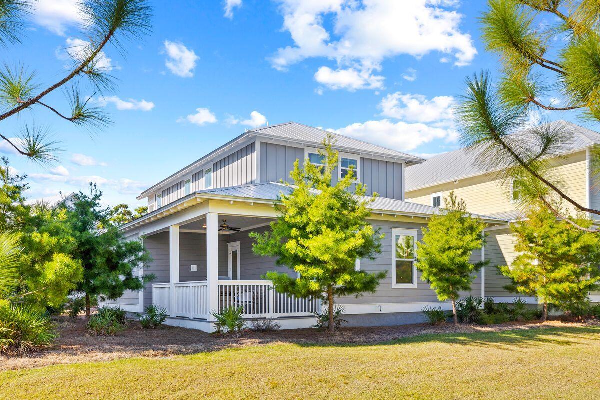 Gray two-story house with a covered porch, white railings, and pine trees in the yard.