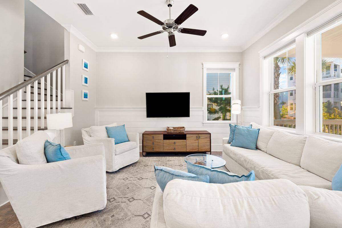 Living room with white seating, blue pillows, a wood media console, and large windows.