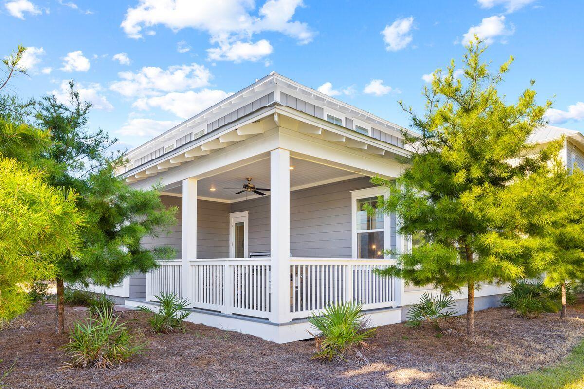 Gray-sided home with a white-trimmed gable and covered front porch among pine trees.