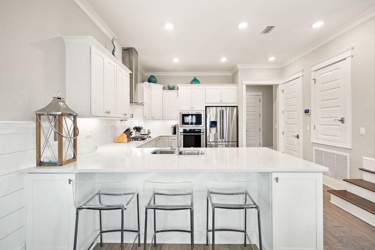 White kitchen with a large island, double-basin sink, three clear stools, and stainless steel appliances.
