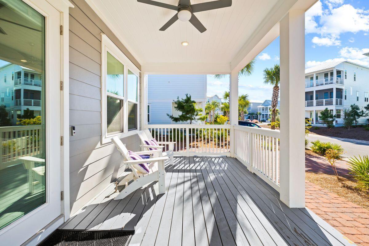 Covered porch with gray decking, white Adirondack chairs, and views of neighboring coastal homes.