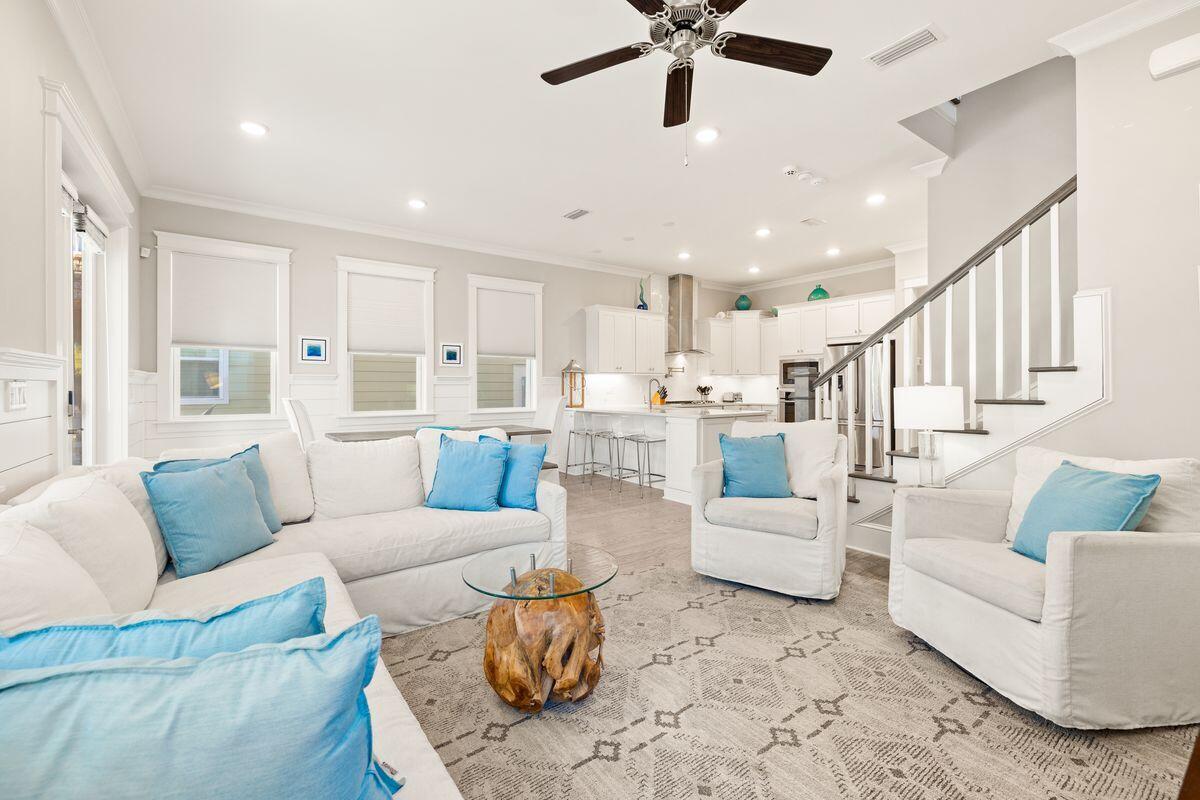 Open-plan living room and kitchen with white seating, blue pillows, and a staircase