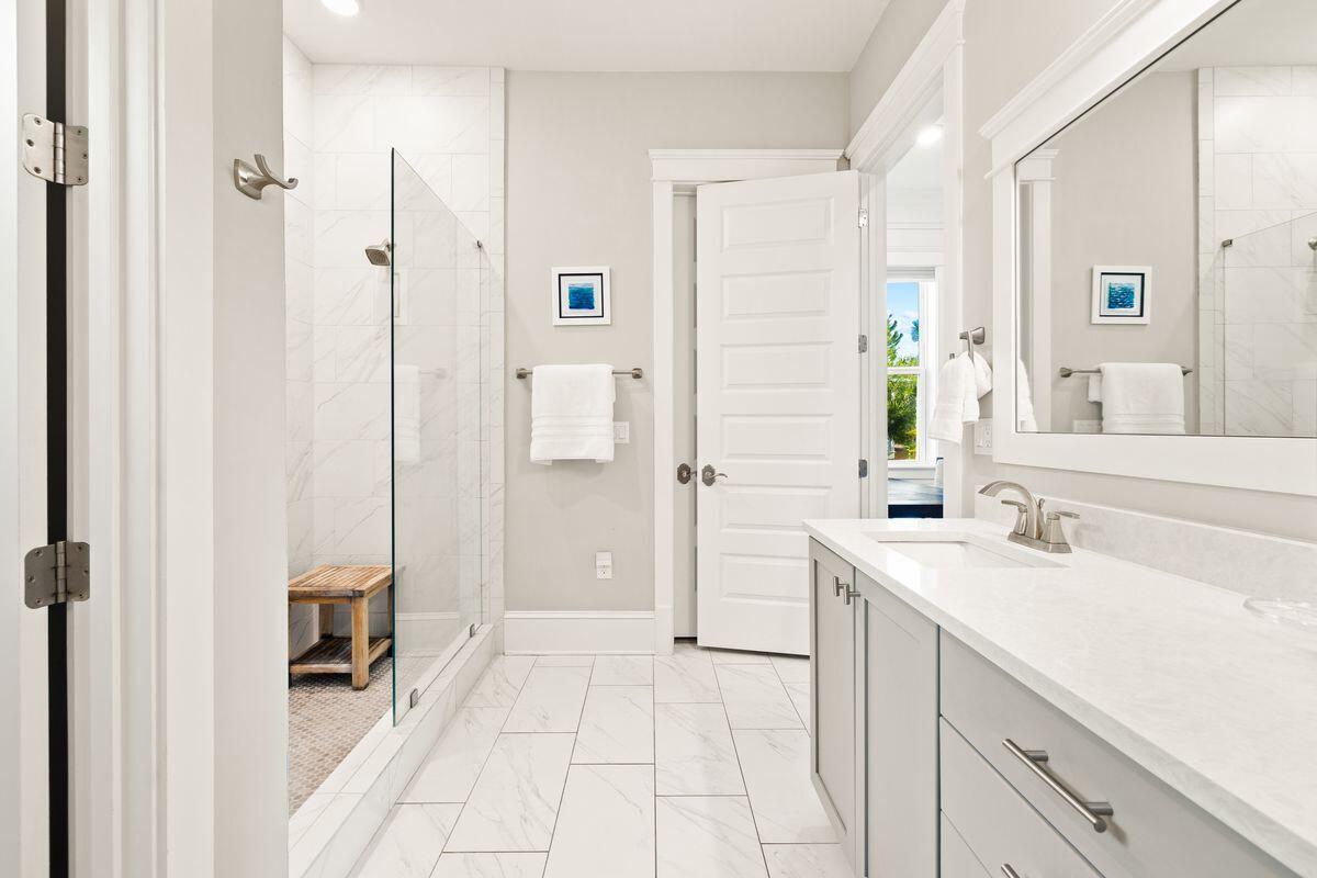 Bathroom with glass shower and wooden bench beside a long white vanity.