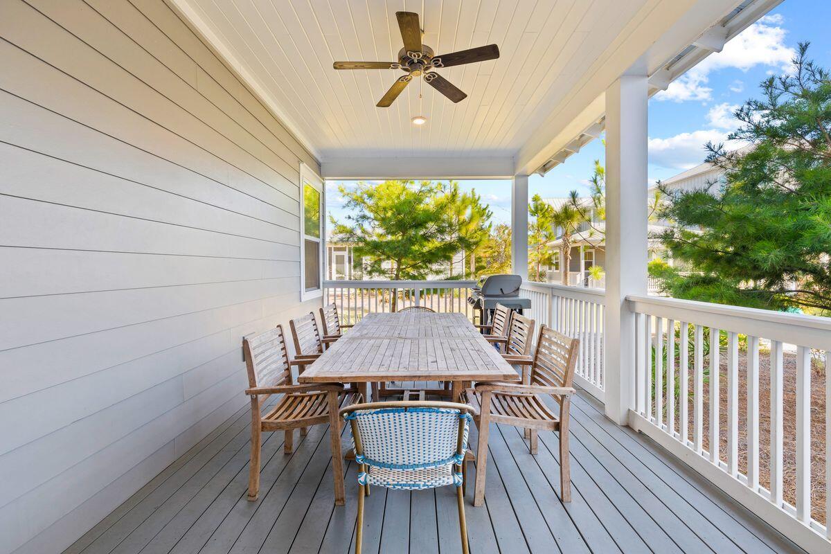Covered porch with a long outdoor dining table, wooden chairs, and a ceiling fan.